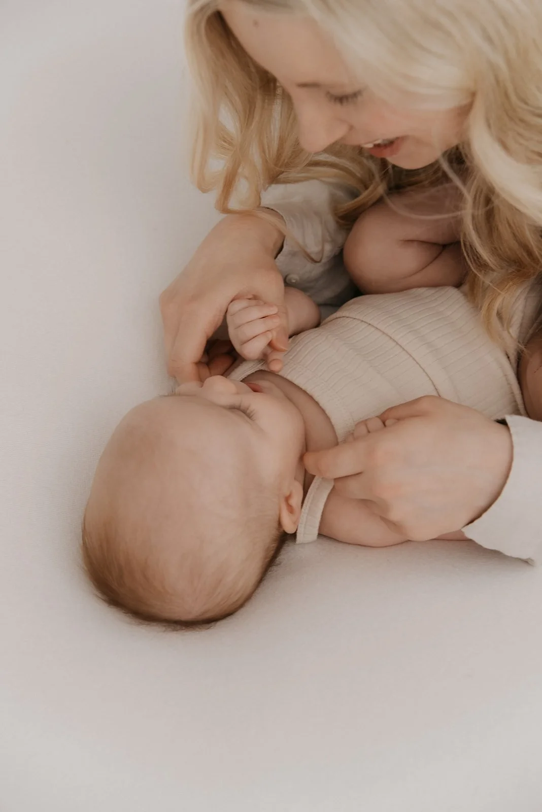 Äiti- ja lapsikuvaus Keravalla harmonisessa studiossa. Äiti hymyilee makaavalle vauvalle.