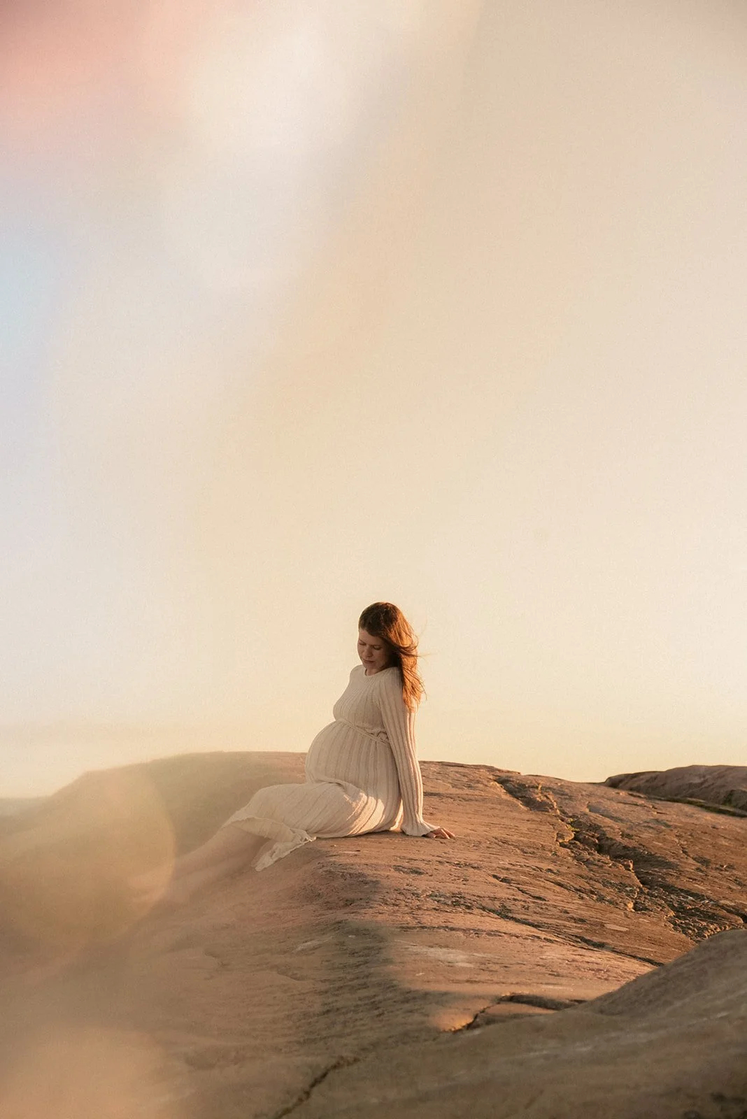 Raskauskuva luonnossa. Odottava äiti istuu kalliolla ilta-auringossa.