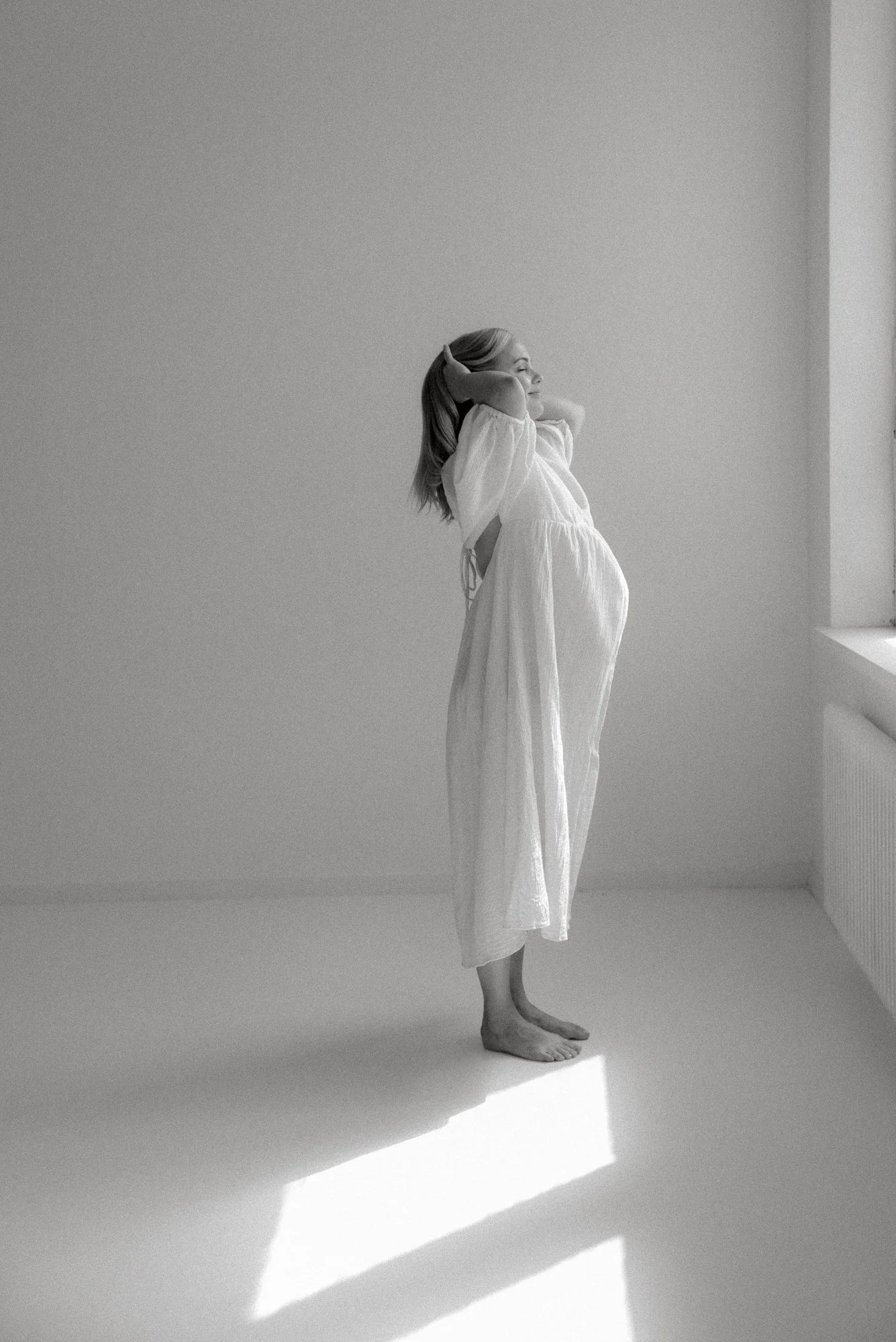 Odotuskuva raskaana olevasta naisesta valoisassa studiossa.