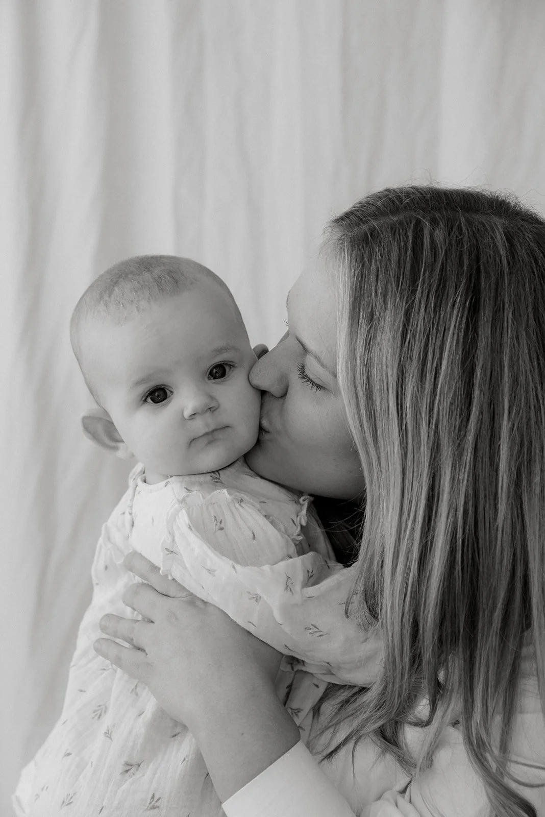 Mustavalkokuva, jossa äiti suukottaa lastaan. Äiti- ja lapsikuvaus, jonka on kuvannut valokuvaaja Heidi Väisänen.