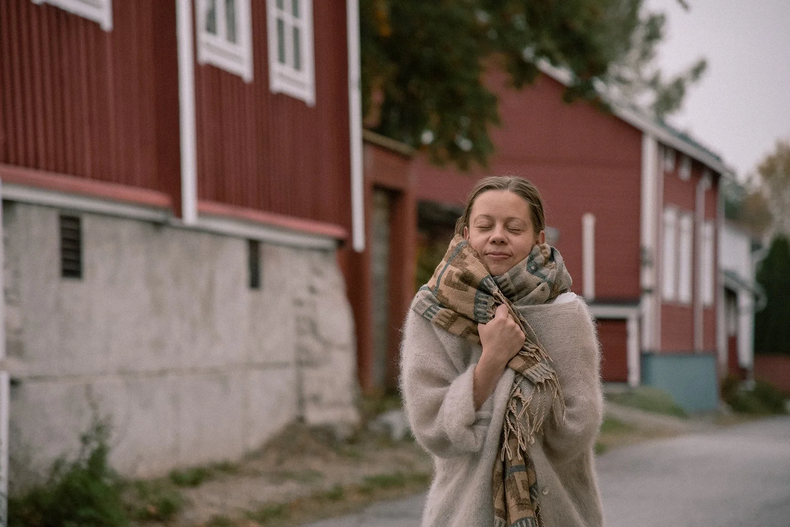 Brändikuvaus keskellä idyllistä puutalomiljöötä. Yrittäjä Laura Laakso kietoutuneena lämpimään huiviin ja neuleeseen.