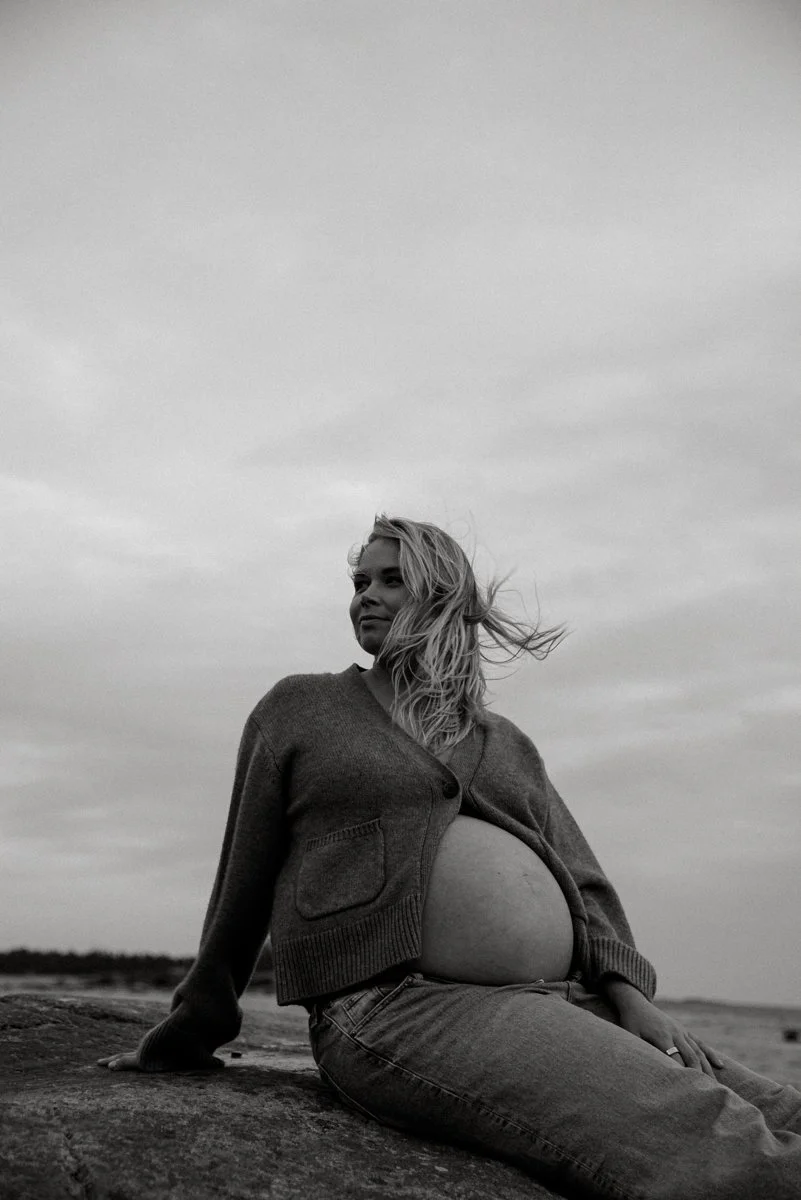 Odottava äiti istuu kalliolla katse pois päin käännettynä. Odotusajankuvaus miljöössä.