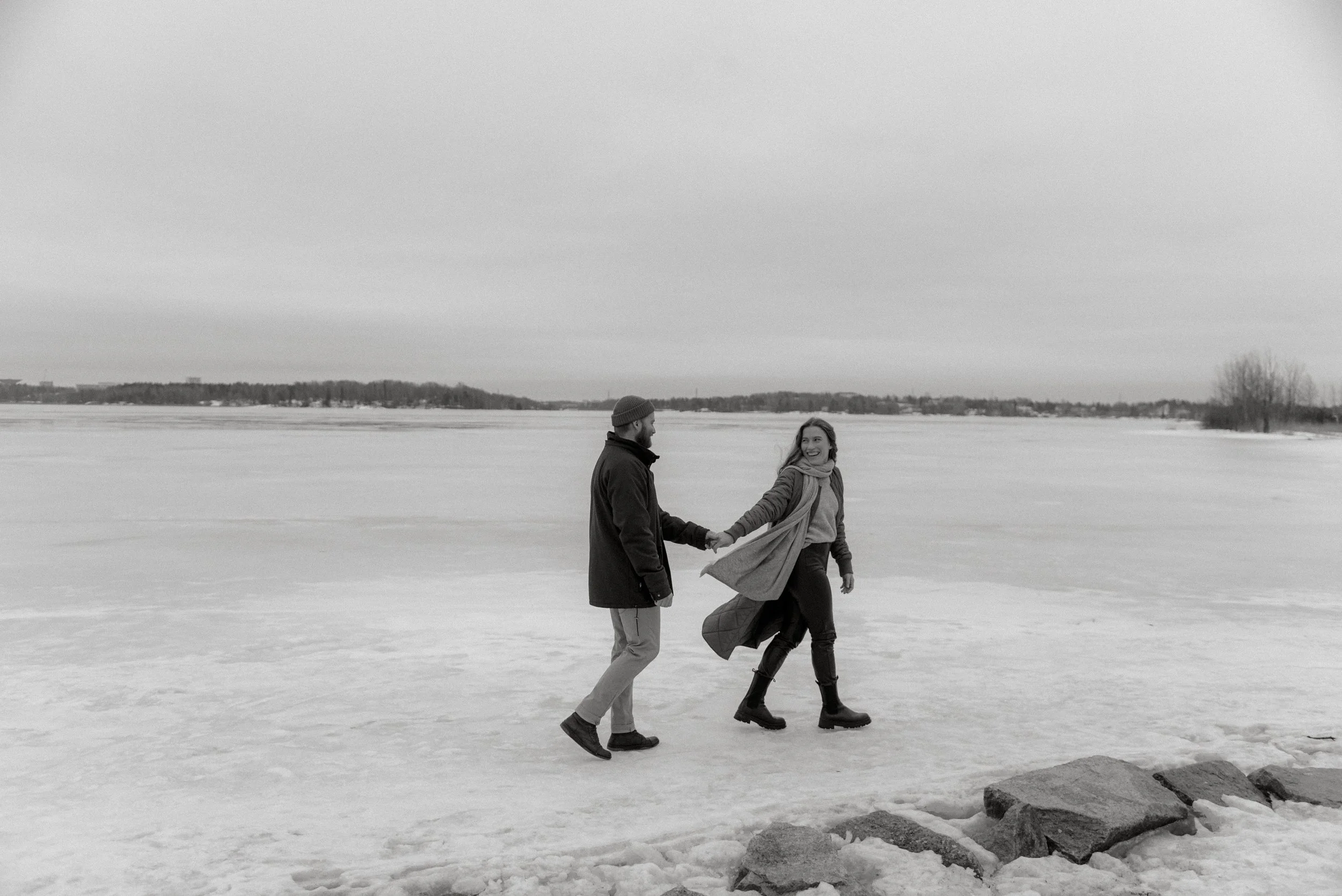 Pariskunta kävelee jäällä ja pitelee toisiaan kädestä. Pariskuntakuvaus Lauttasaari.