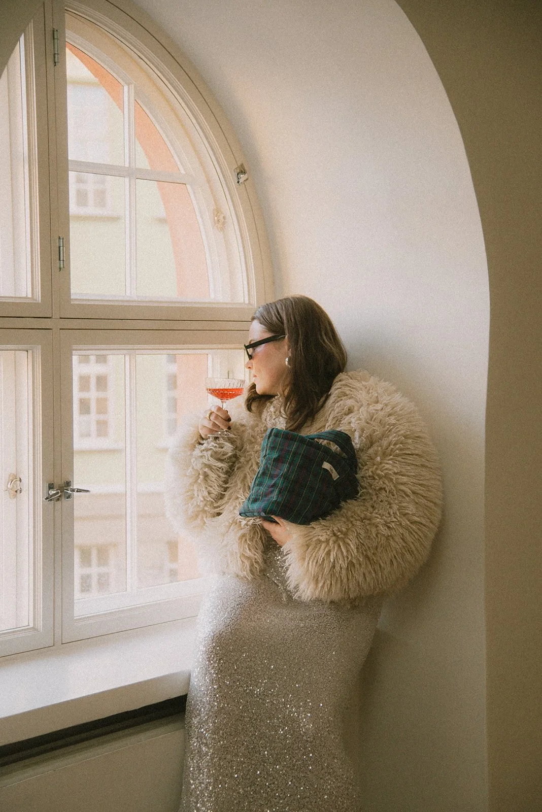 Naisyrittäjä katsoo ikkunasta ulos lasi kädessään. Kuvannut henkilökuvaaja Heidi Väisänen.