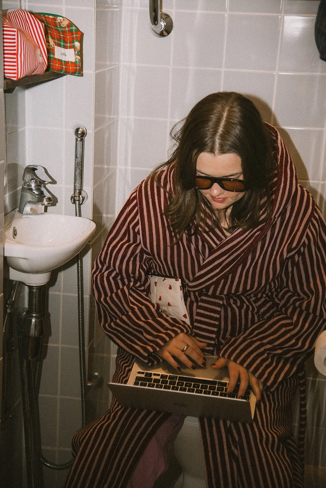 Nainen näpyttelee tietokonetta kylpyhuoneessa kylpytakki päällään. Kuvannut yrityskuvaaja Heidi Väisänen.