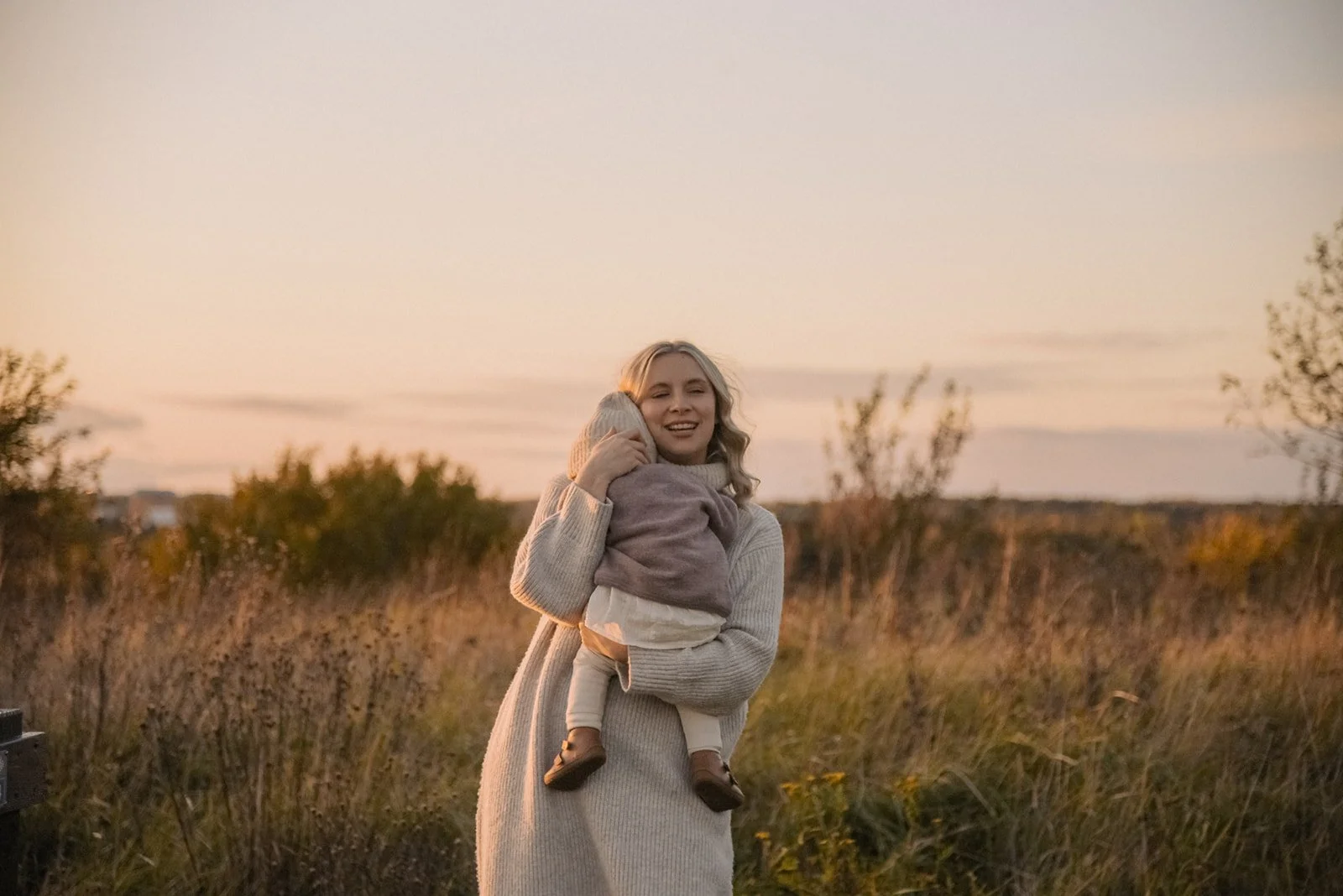 Perhekuvaus luonnossa, äiti ja pitää pientä lasta sylissään ilta-auringossa. Kuvannut perhekuvaaja Heidi Väisänen.