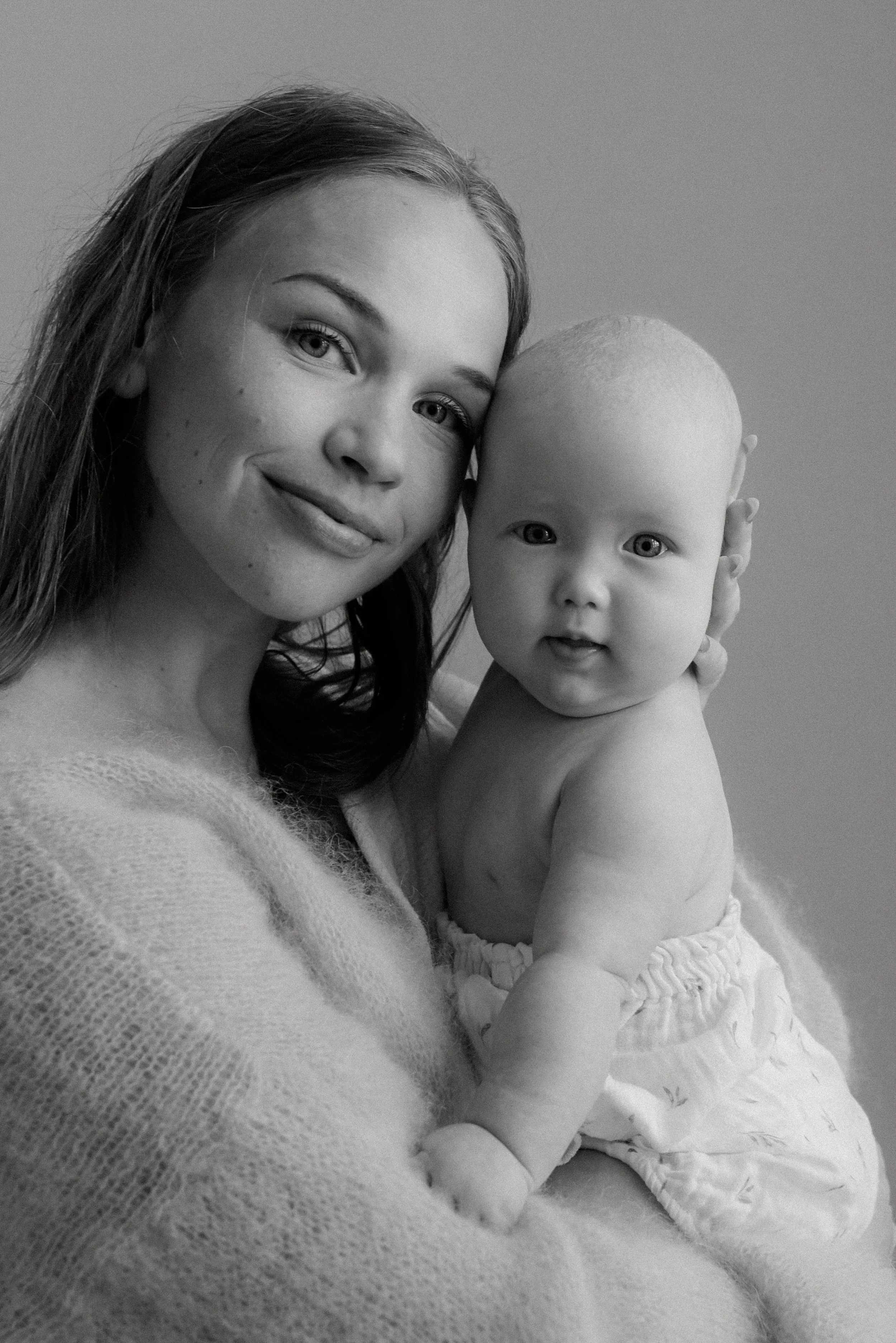 Lähikuvassa äiti sekä vauva katsovat suoraan kameraan. Äiti- ja lapsikuvaus studiossa.