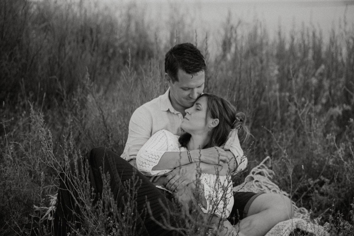 Pariskunta istuu ruohikossa sylikkäin. Kuvannut perhekuvaaja Heidi Väisänen.
