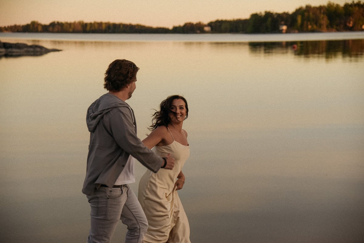 Iloinen pariskunta juoksee veden äärellä. Pariskuntakuvaus Espoo.
