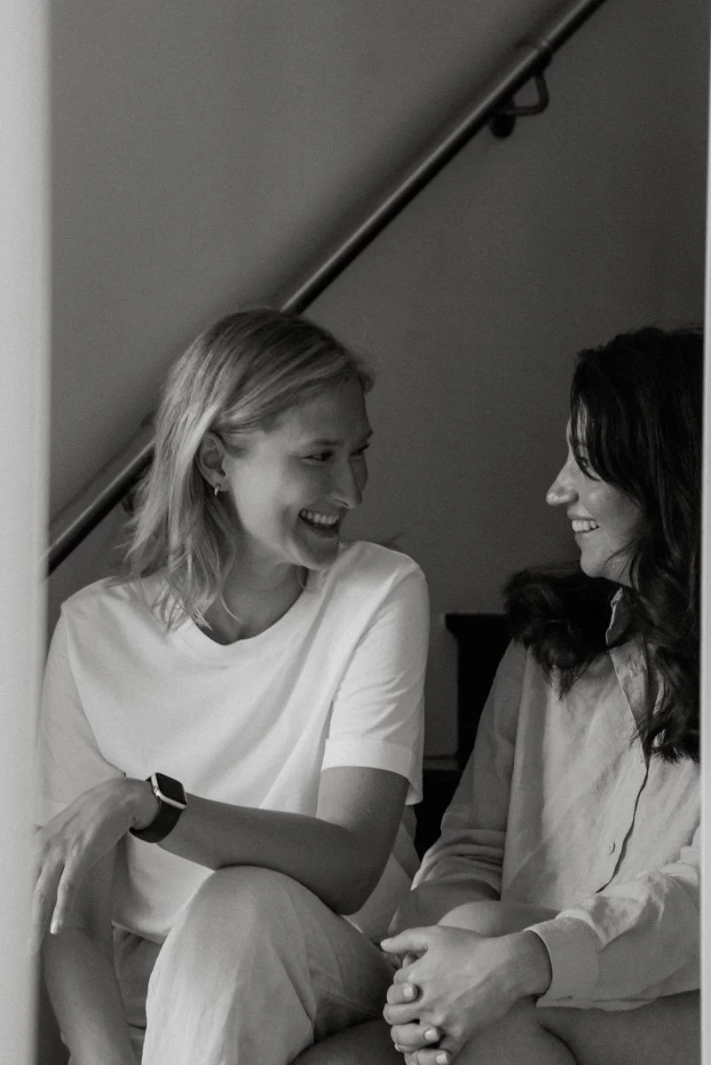 Neam Societyn brändikuvaus, naisyrittäjät istuvat portaissa ja katsovat hymyillen toisiaan.