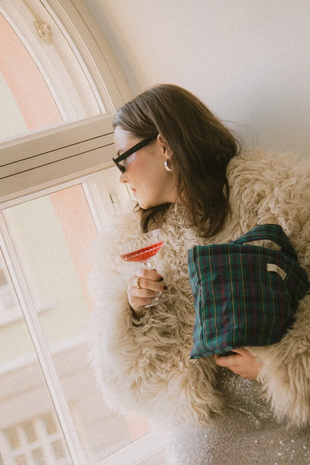 Naisyrittäjä katsoo ikkunasta ulos lasi kädessään. Kuvannut henkilökuvaaja Heidi Väisänen.