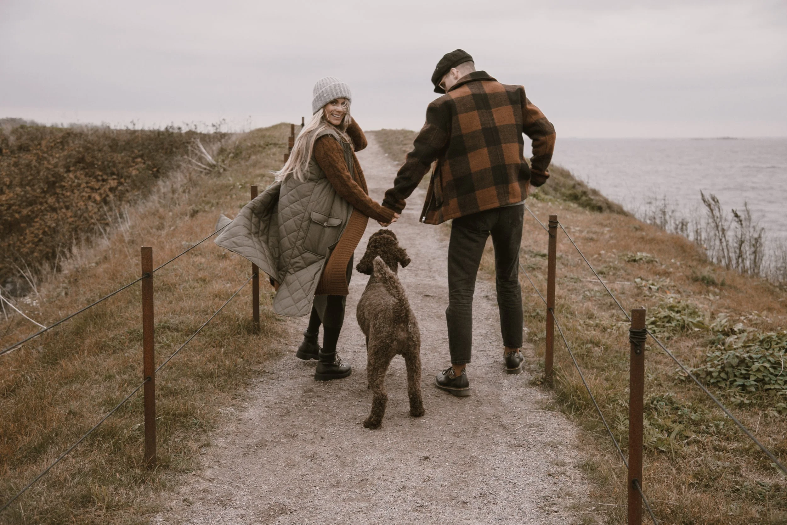 Hiekkatietä käsi kädessä kävelevä pariskunta ja koira. Odotusajankuvaus on toteutettu Suomenlinnassa.
