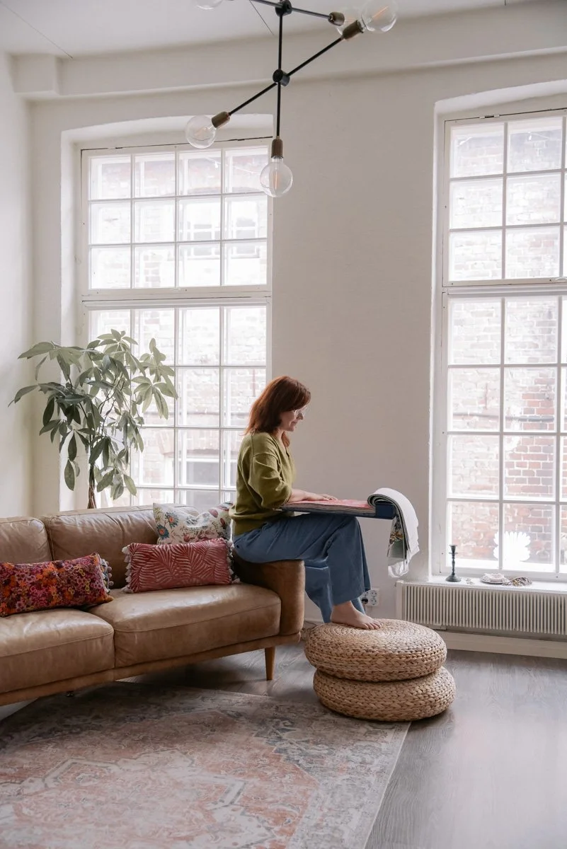 Verhoomo Vanhan Viehätys brändikuvaus, yrittäjä Virve Taljavirta istuu sohvalla kauniissa toimitilassaan ja pitelee käsissään kangasnäytteitä.