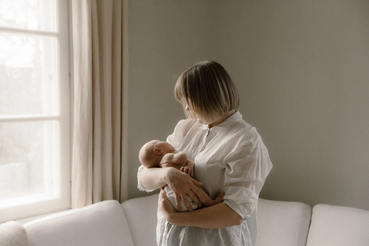 Perhekuvaus kotimiljöössä. Äiti pitää vauvaa sylissään.