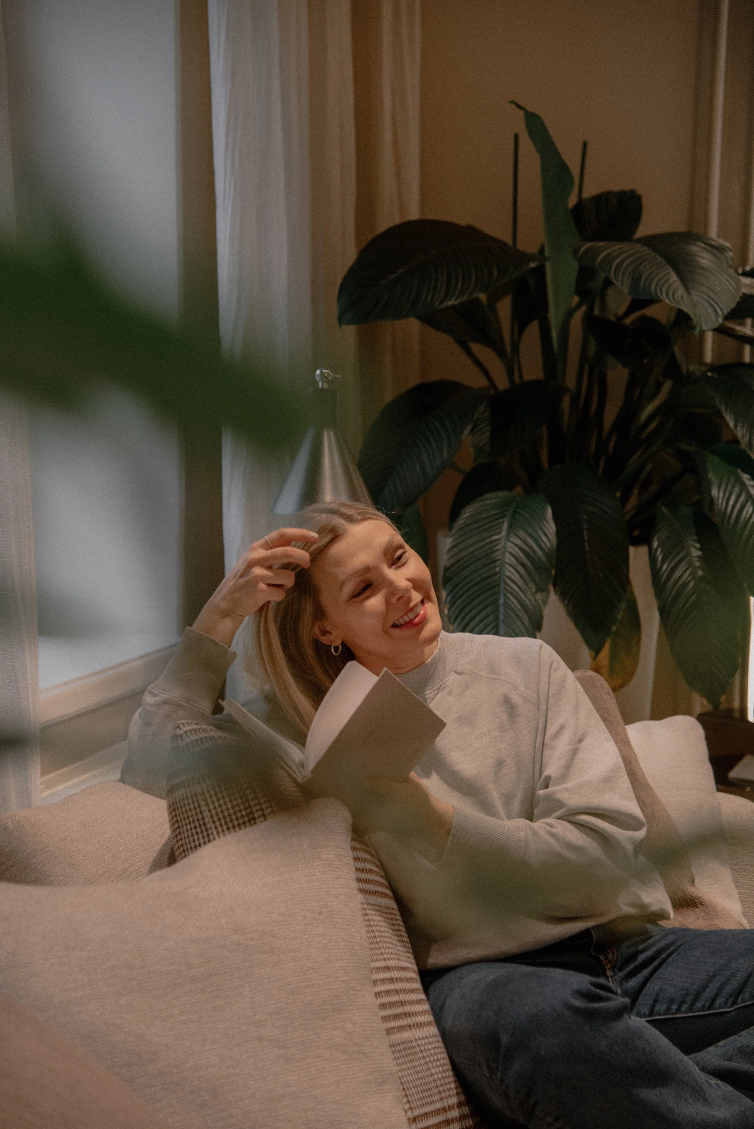 Onnellinen naisyrittäjä istuu vaalealla sohvalla olohuoneessa.