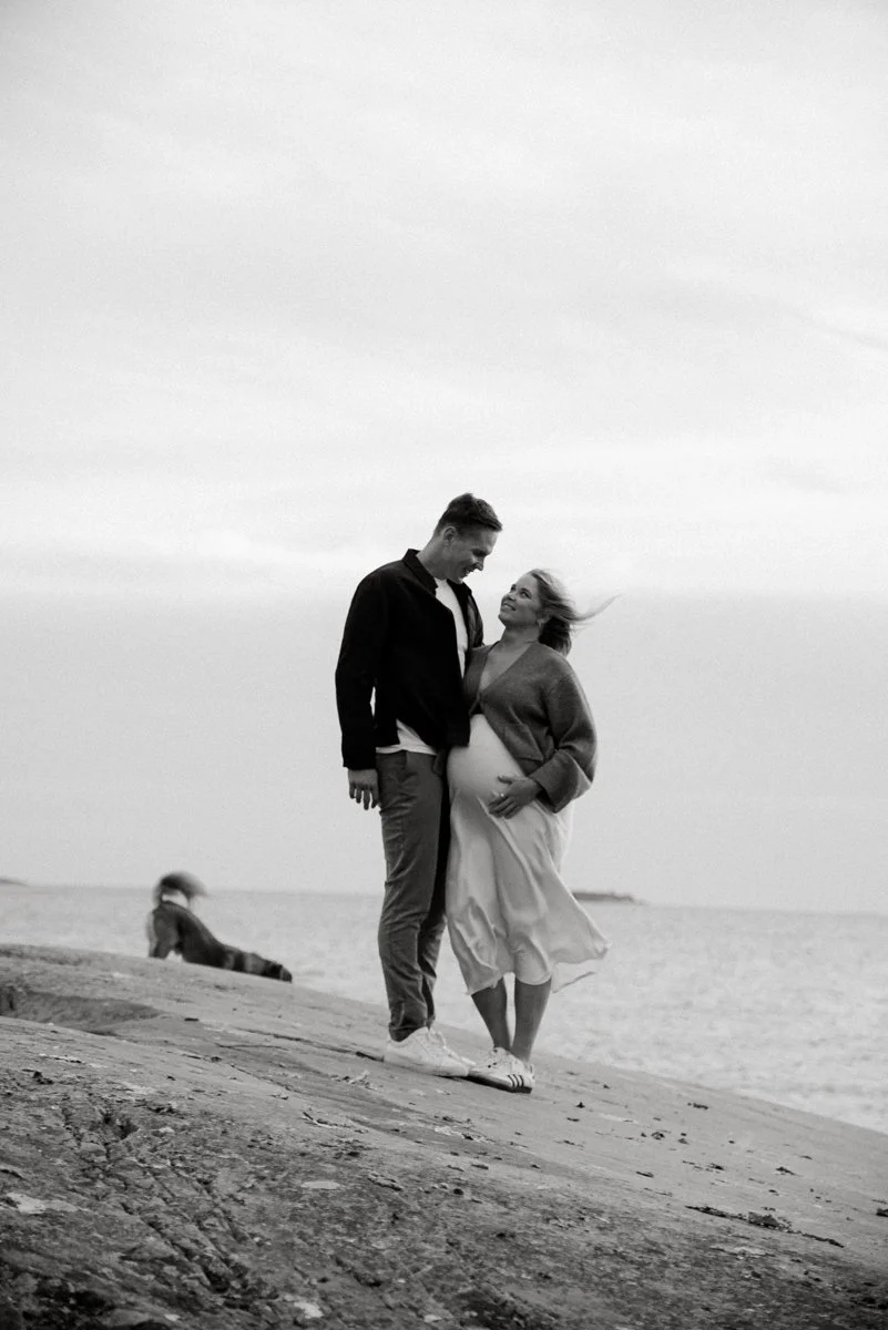 Minimalistinen valokuva, jossa vauvaa odottava pariskunta ja taustalla koira.