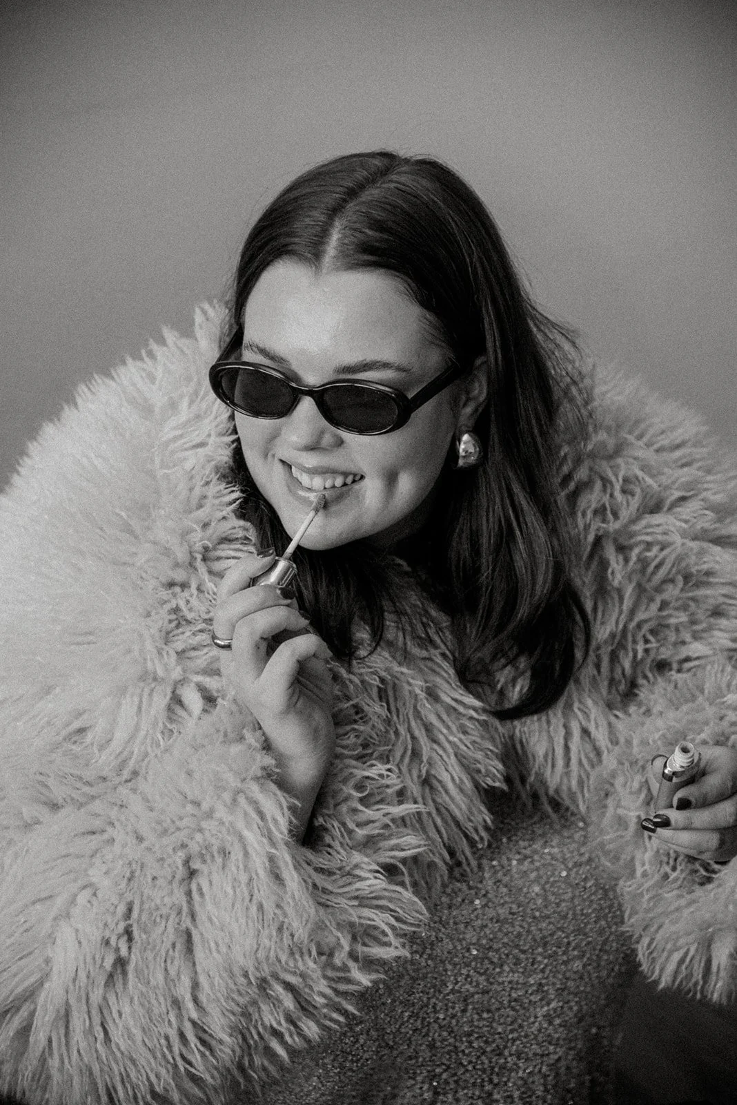 Mustavalkoinen henkilökuva. Edlan yrittäjä sipaisee huulikiiltoa aurinkolasit päässään.