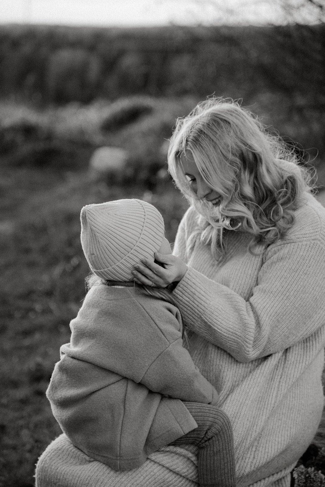 Idyllinen mustavalkoinen perhekuva, jossa äiti katsoo lempeästi sylissään istuvaa pientä lasta.