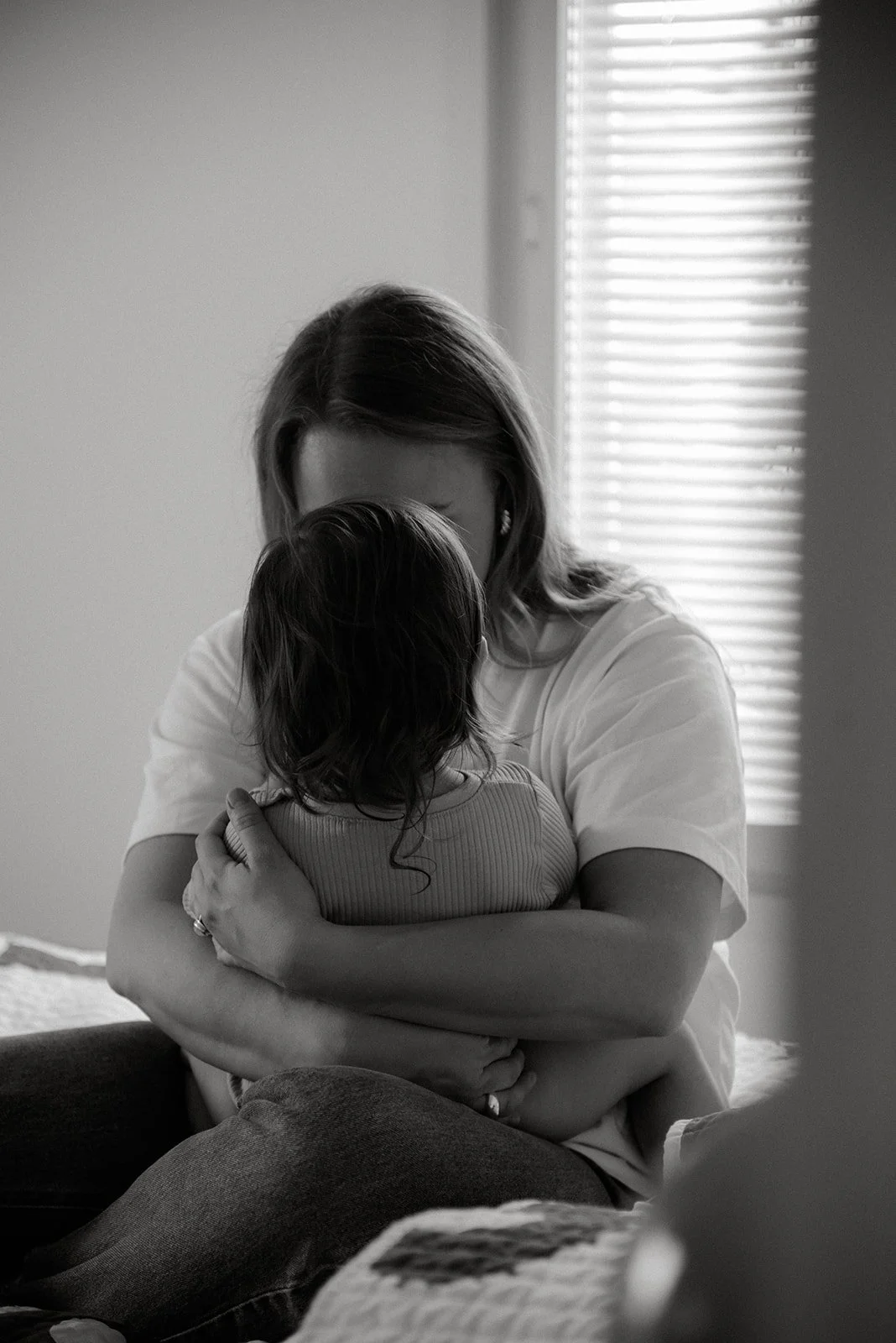 Mustavalkoinen perhekuva, jossa äiti halaa lastaan.