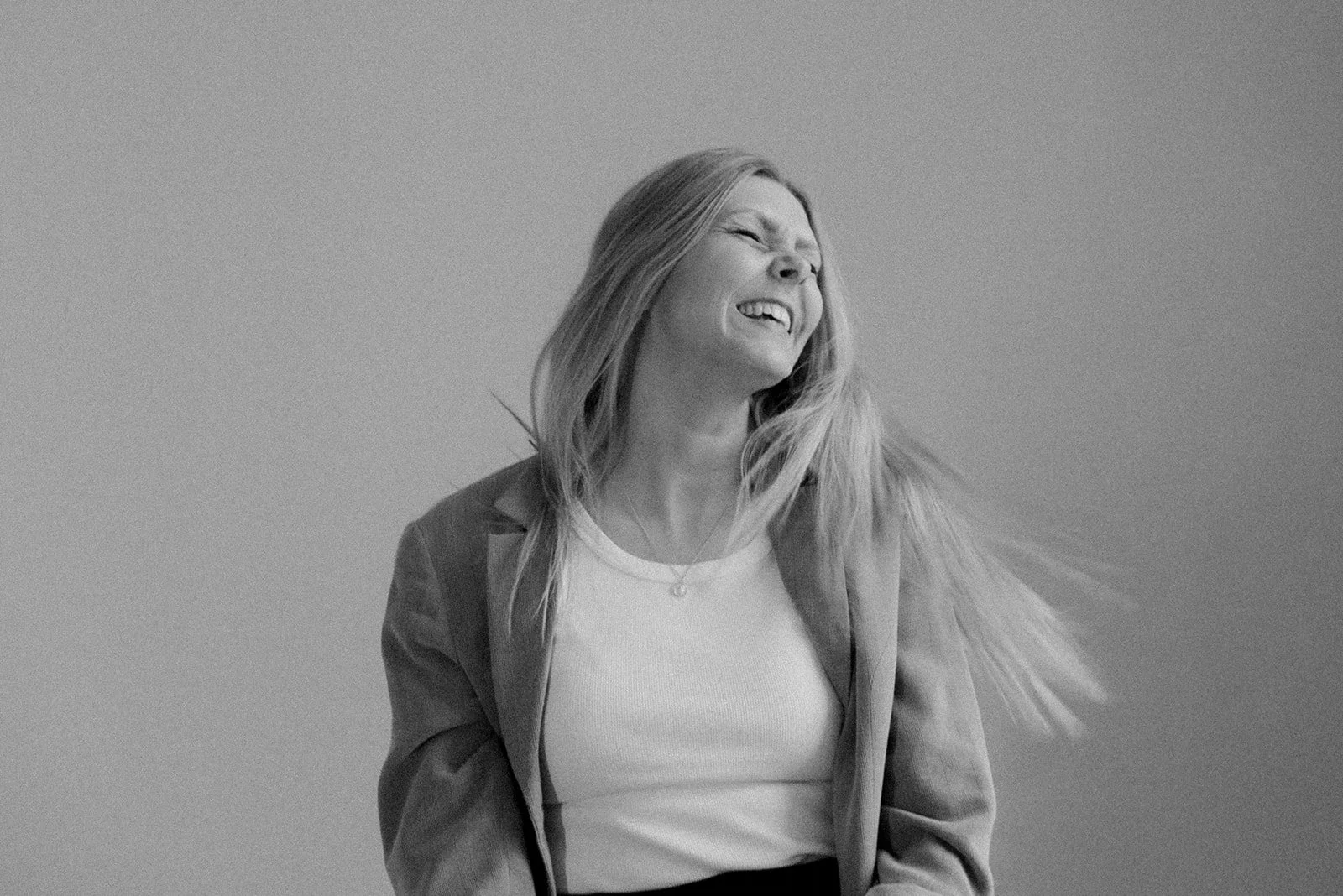 Heartiven yrityskuvaus, iloinen naisyrittäjä heilauttaa päätään mustavalkokuvassa.