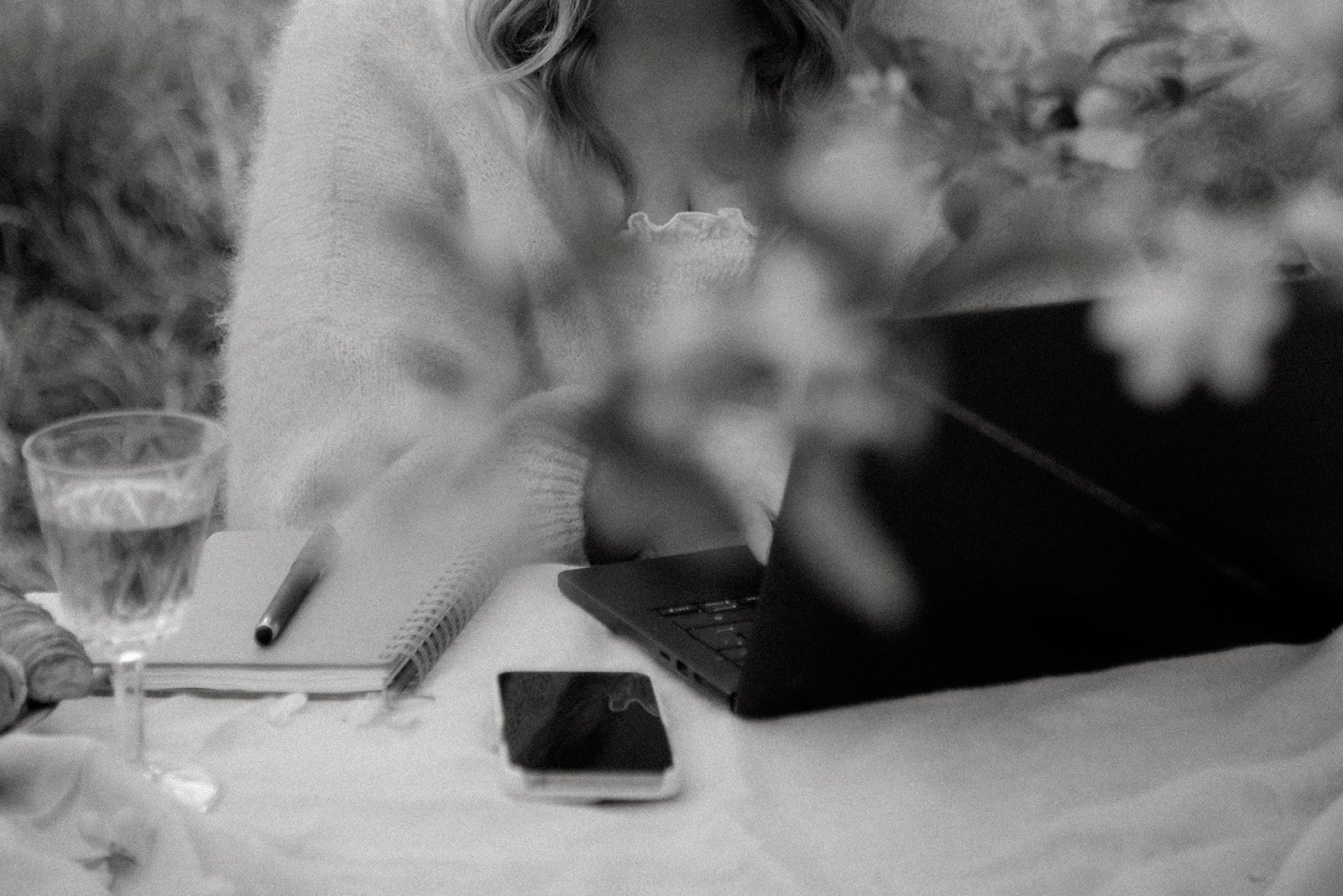 Yrityskuvaus luontomaisemassa. Naisyrittäjä näpyttelee tietokonetta, vieressä lasi, muistikirja ja kännykkä.