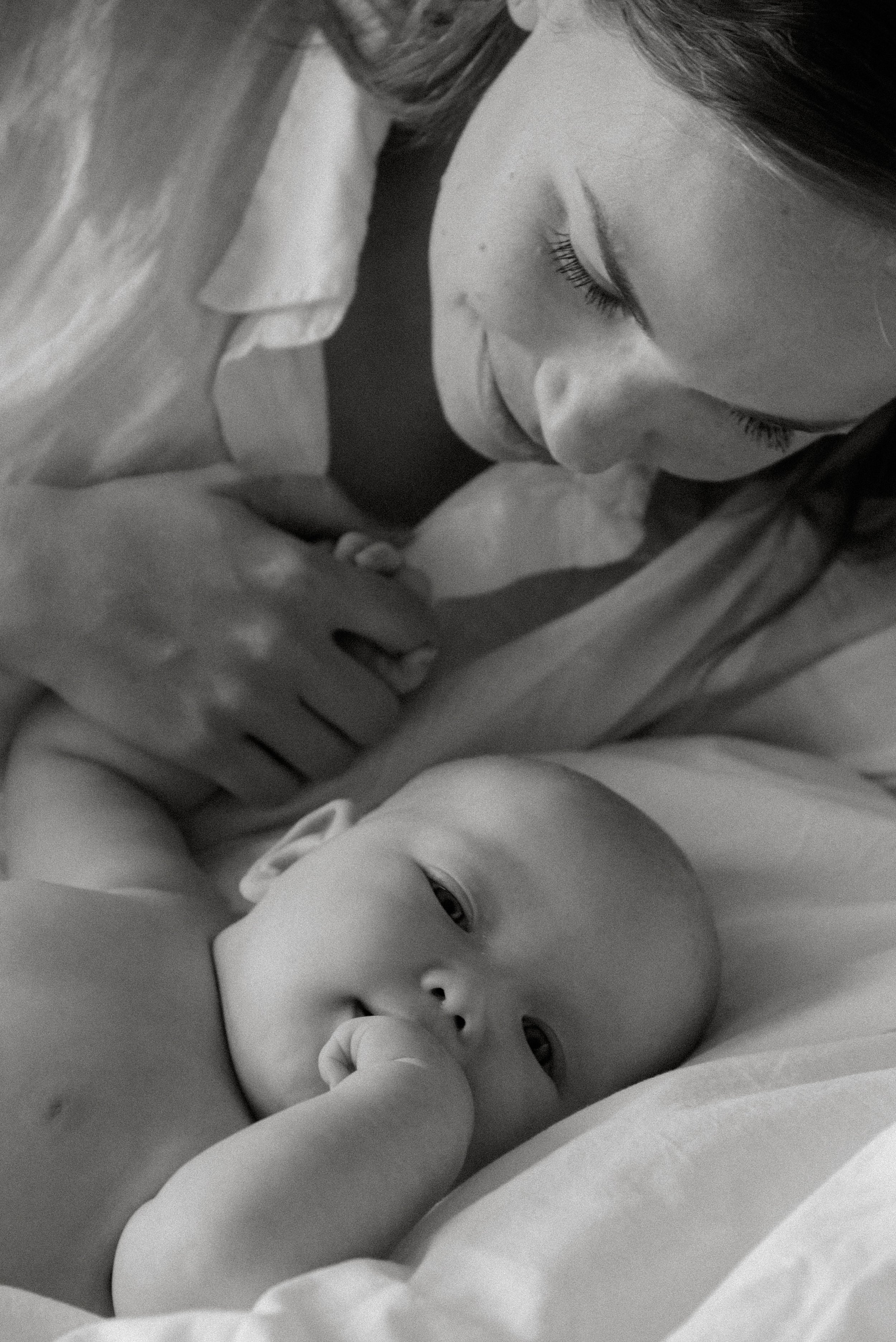 Mustavalkoinen lähikuva äidistä ja vauvasta Heidi Väisäsen valokuvastudion sängyllä.