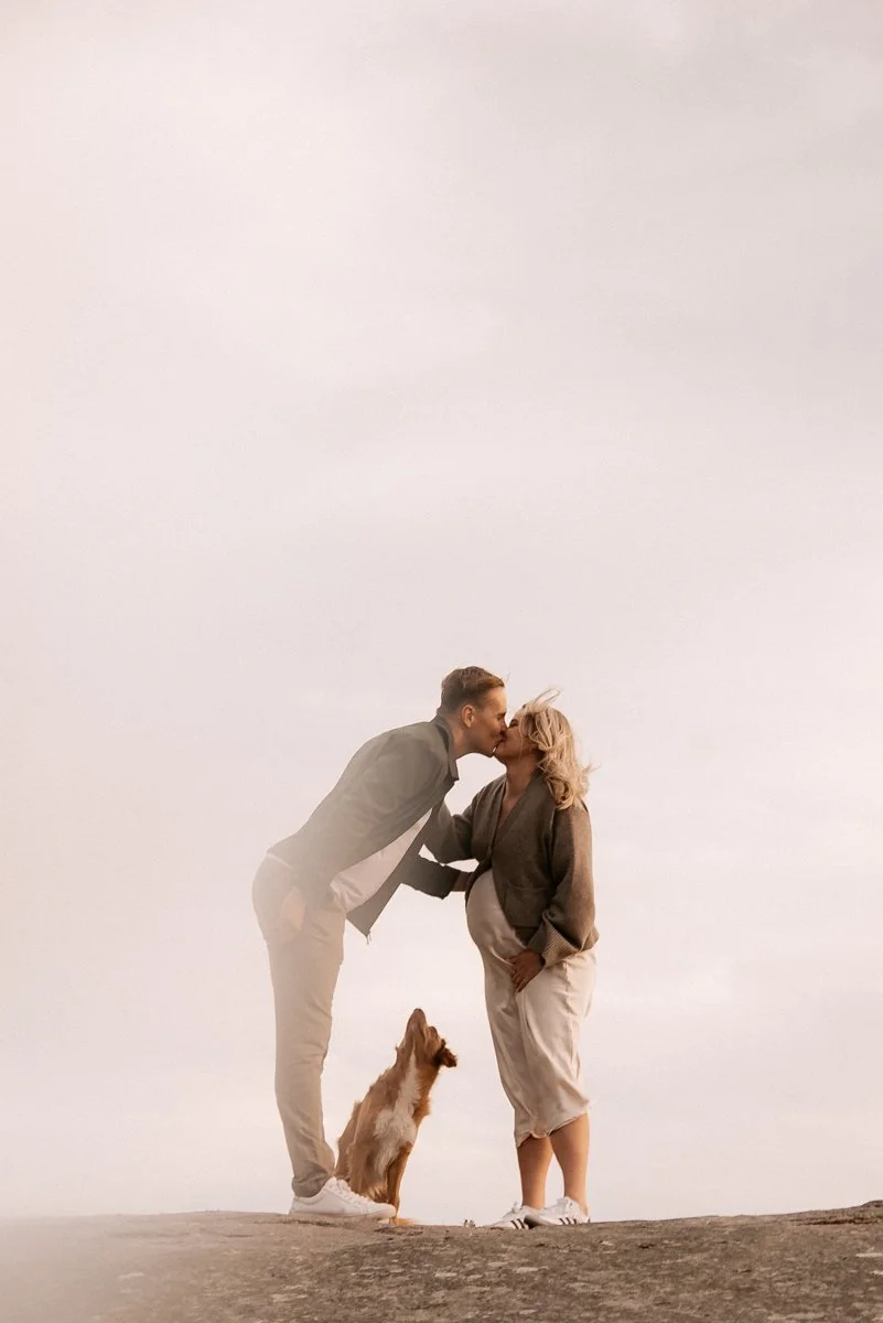 Lasta odottava pariskunta koiran kanssa luonnossa kuvattuina.