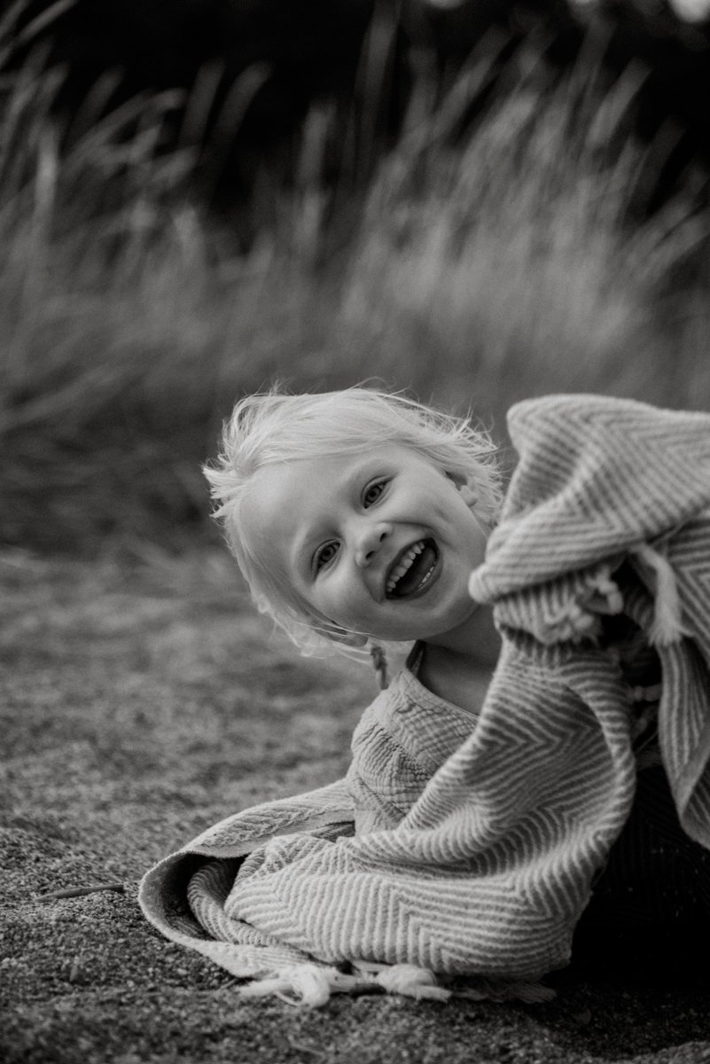 Nauravainen lapsi vilttiin kääriytyneenä rannalla.