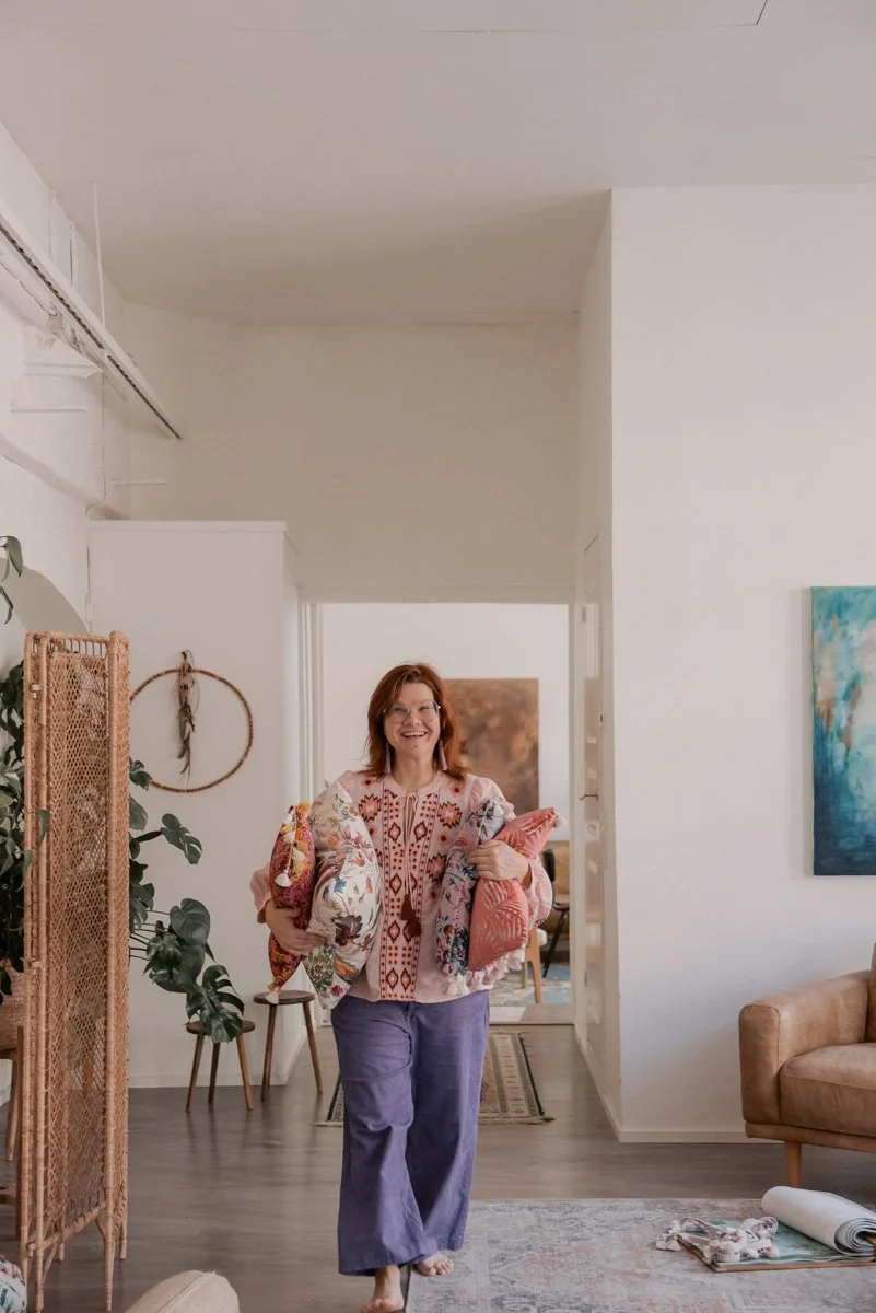 Verhoomo Vanhan Viehätys brändikuvaus, yrittäjä Virve Taljavirta kantaa kainaloissaan värikkäitä tyynyjä.