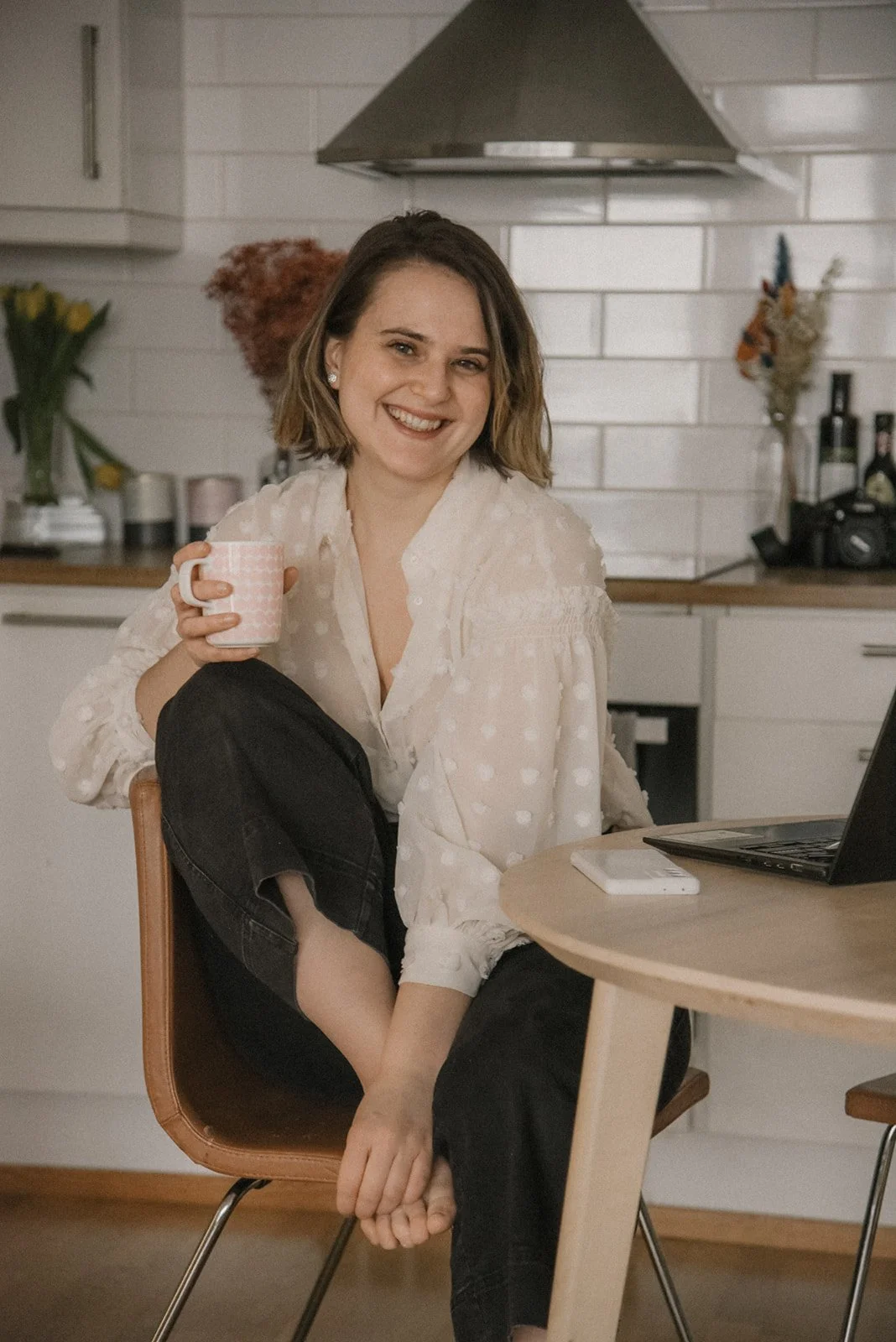 Kuvaus kotona -kuvauksessa iloinen äiti keittiönpöydän ääressä kahvikuppi kädessä.