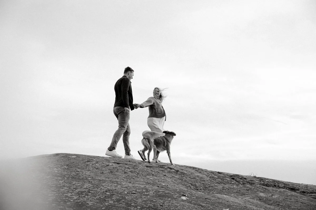Isä, raskaana oleva äiti ja koira kävelevät pitkin kalliota yhdessä.