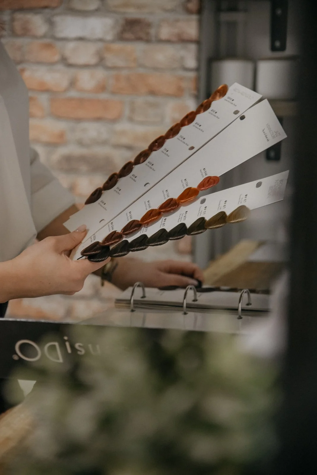 Brändikuvaus kampaamossa, kampaaja selaa värikarttaa.