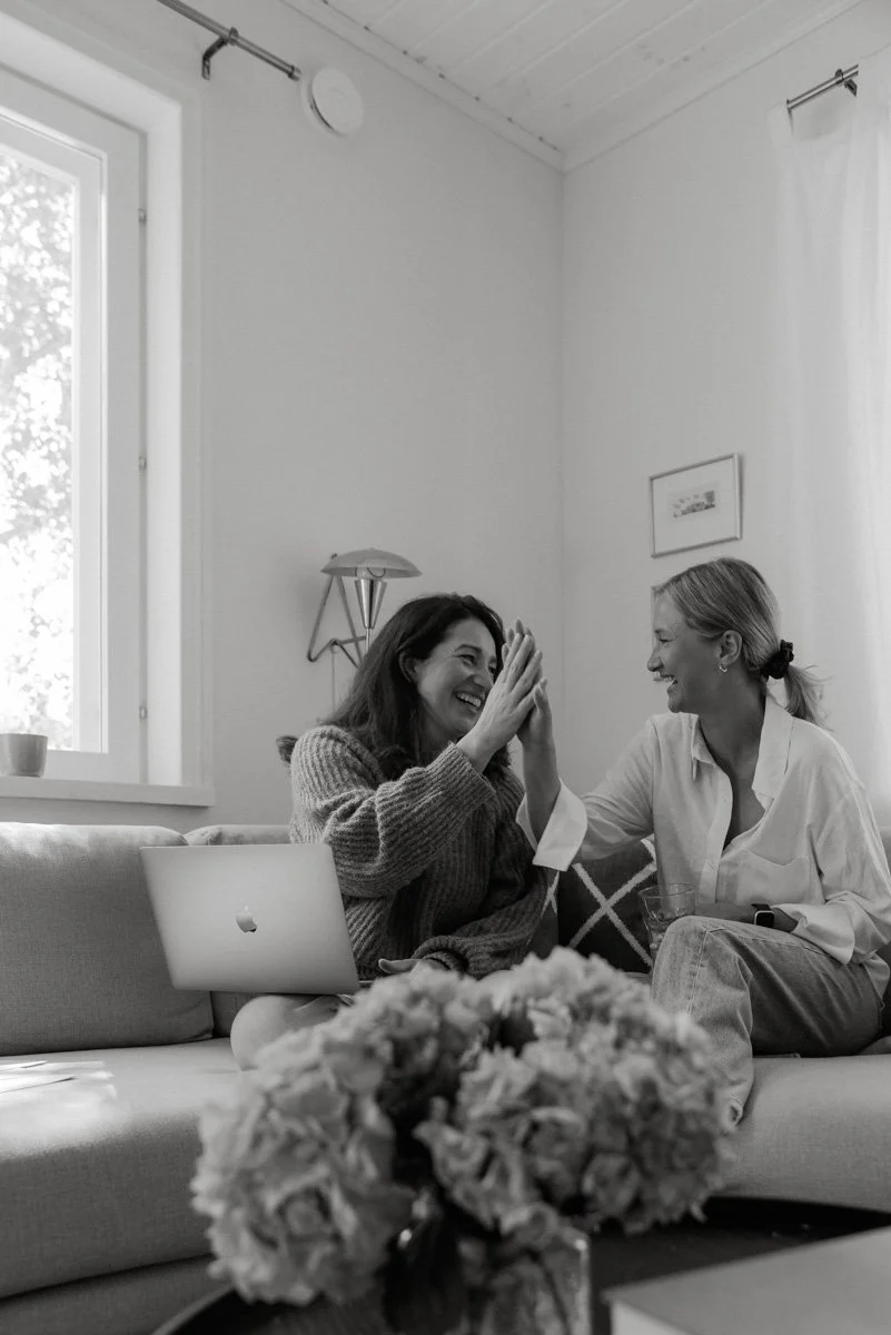 Neam Societyn brändikuvaus, naisyrittäjät hymyilevät toislleen sohvalla.