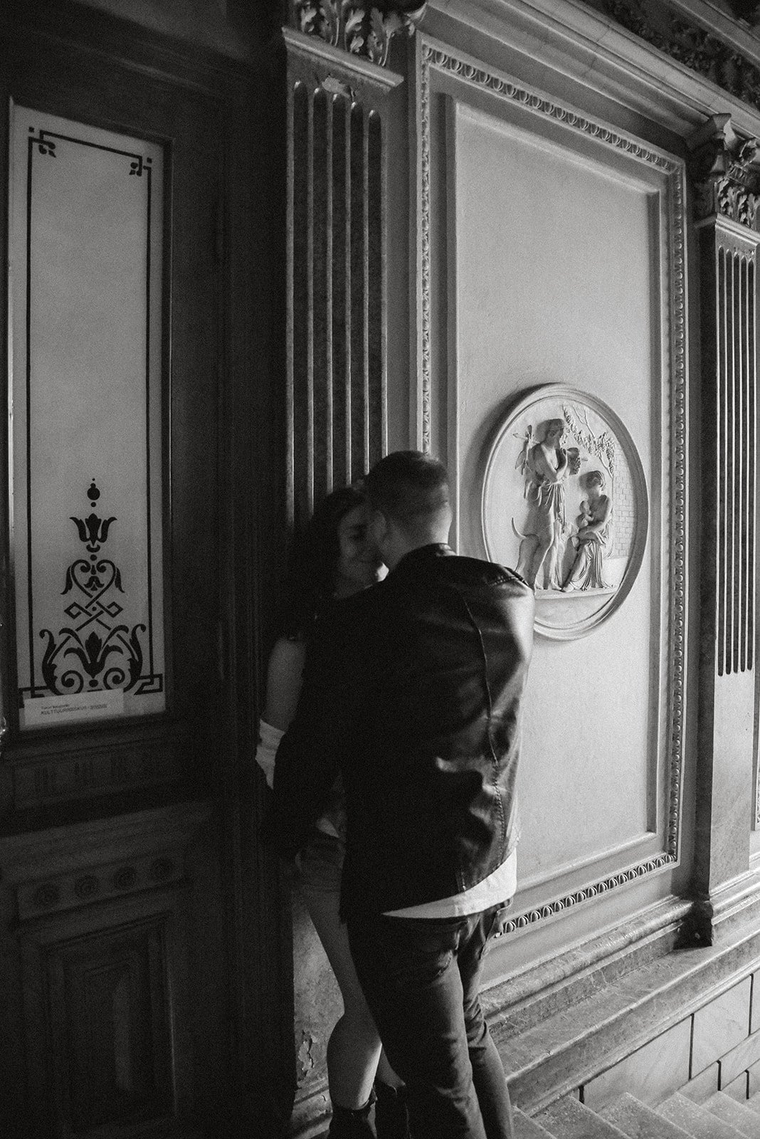 Mustavalkoinen pariskuntakuva, jonka on ottanut valokuvaaja Heidi Väisänen. Nainen ja mies seisovat lähekkäin kauniissa rappukäytävässä.