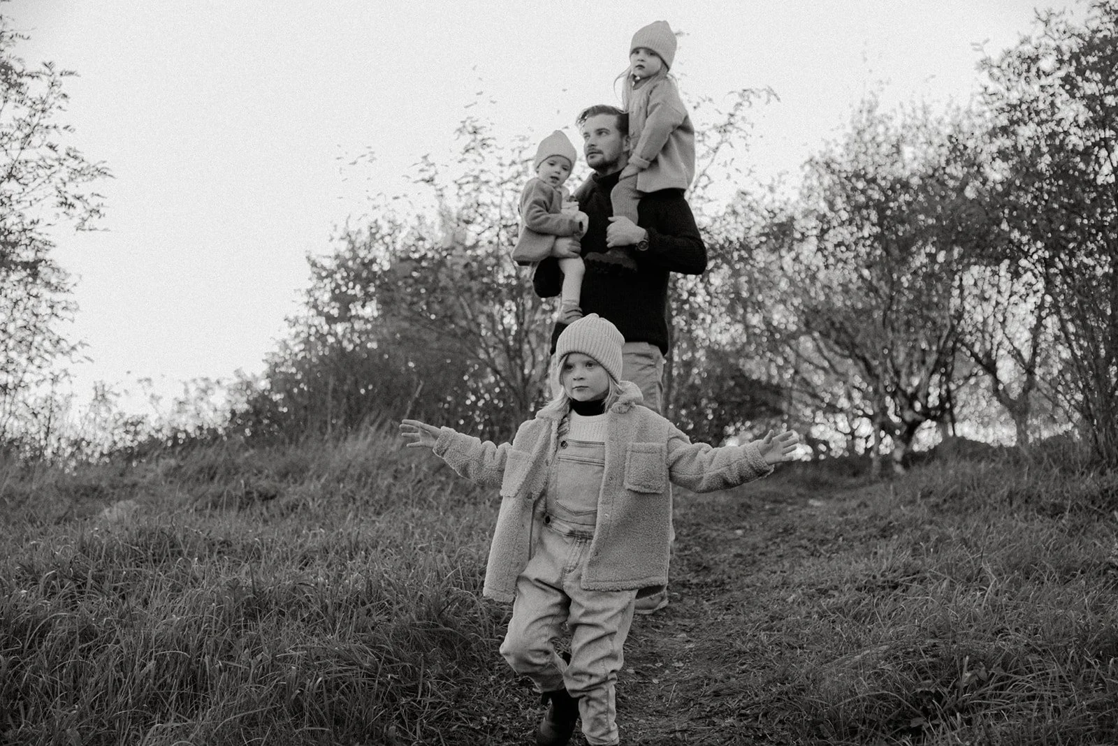 Mustavalkoinen kuva isästä ja kolmesta lapsesta. Perhekuvaus luontokohteessa.