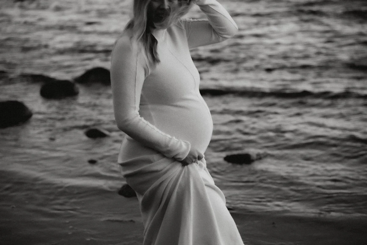 Odottava äiti kävelee veden rajaa pitkin. Odotusajankuvaus luontomaisemassa.