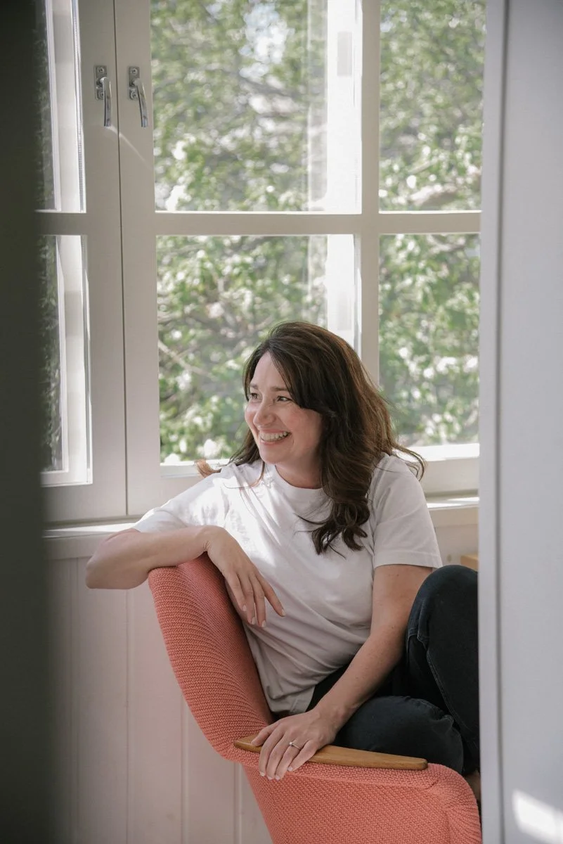Neam Societyn yrittäjä hymyilee iloisesti nojatuolissa. Kuvannut henkilökuvaaja Heidi Väisänen.