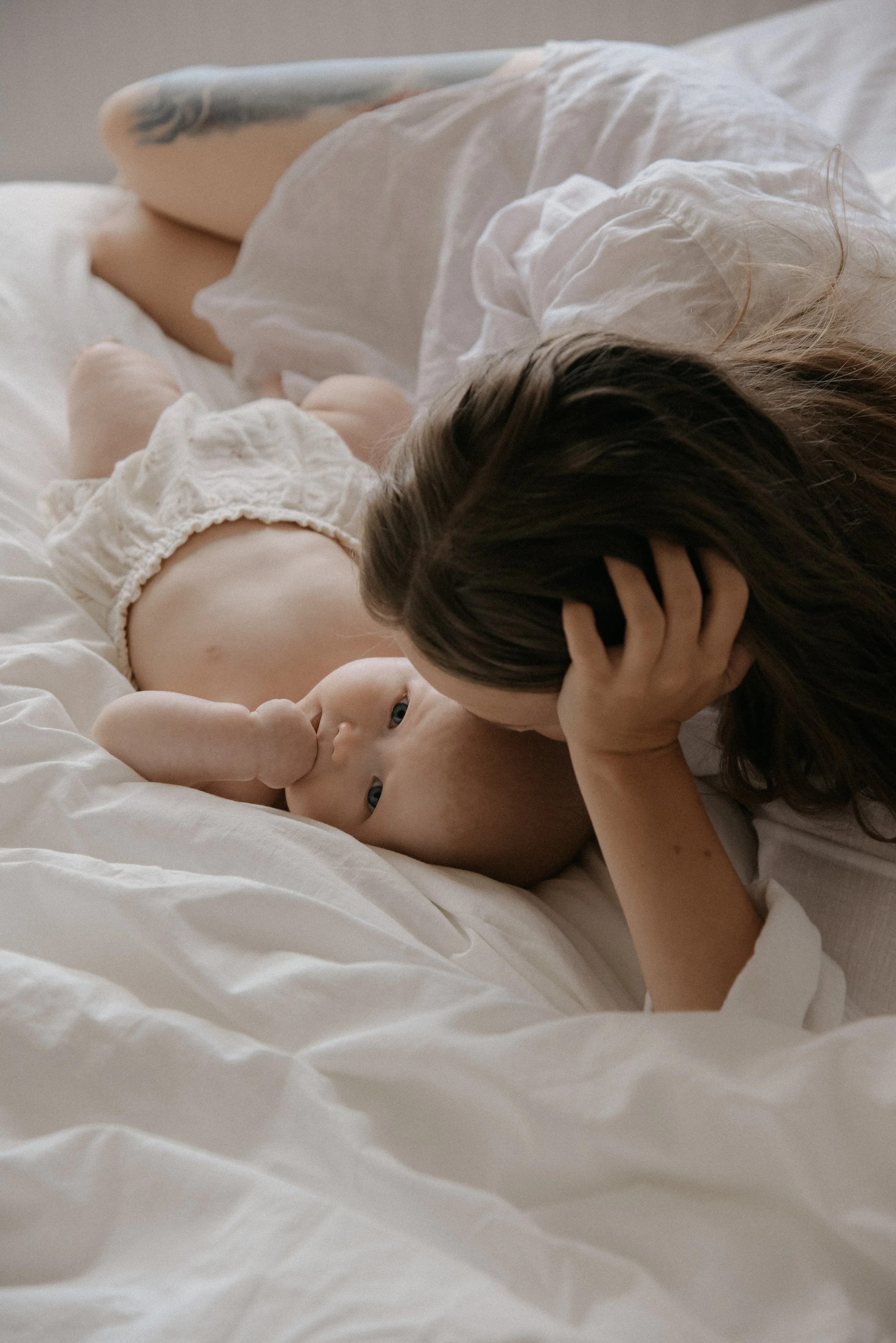 Äiti ja vauva makoilevat rennosti sängyllä. Äiti- ja lapsikuvauksen on toteuttanut Heidi Väisänen.