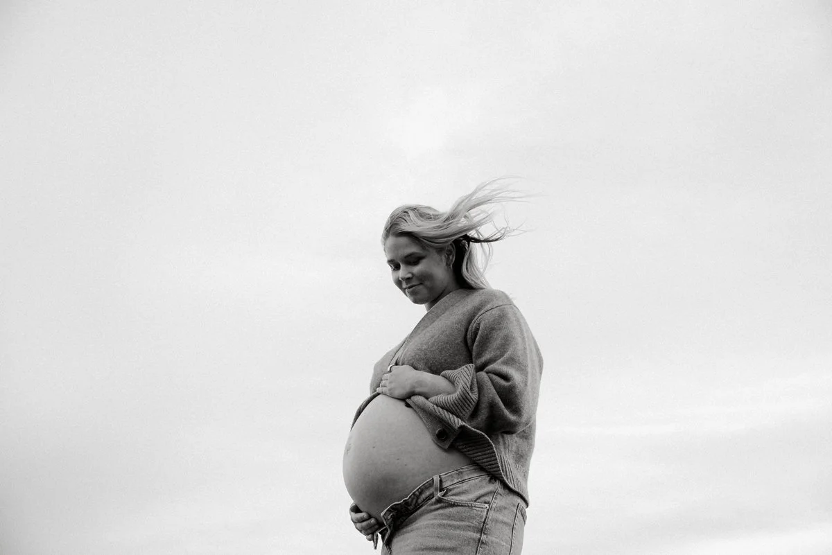 Raskauskuva odottavasta äidistä, joka pitelee vatsaansa taivas taustalla.