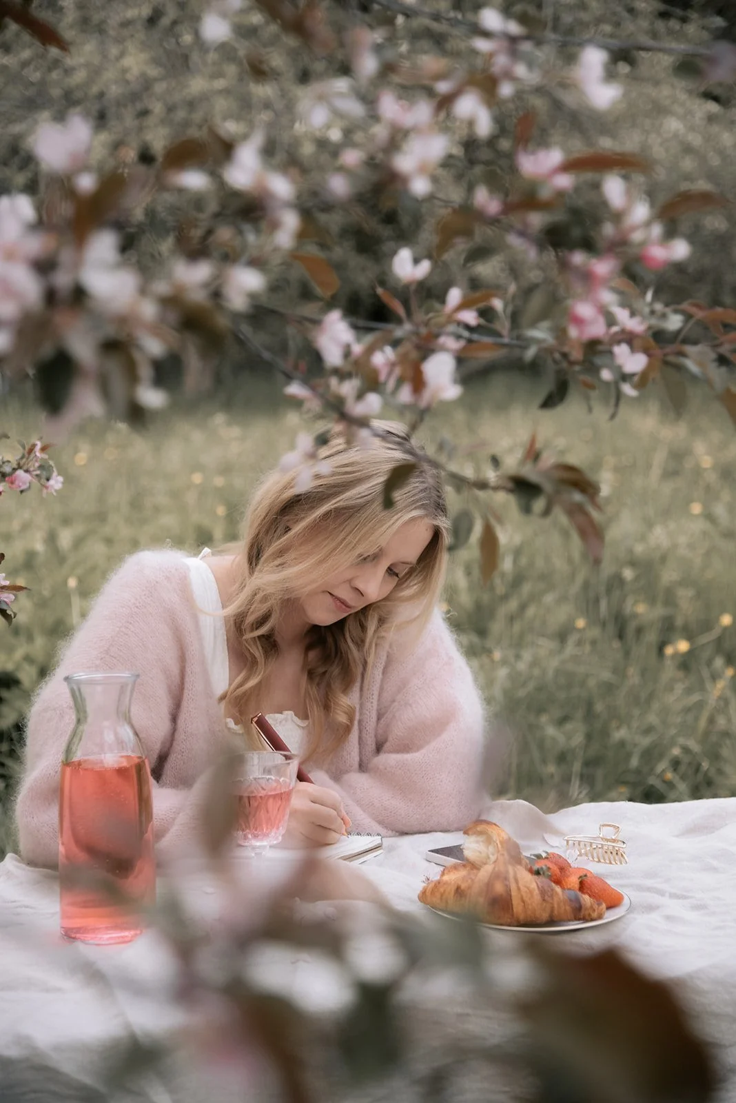 Brändikuvaus kirsikkapuiden keskellä. Naisyrittäjä istuu pöydän ääressä ja kirjoittaa muistikirjaansa.