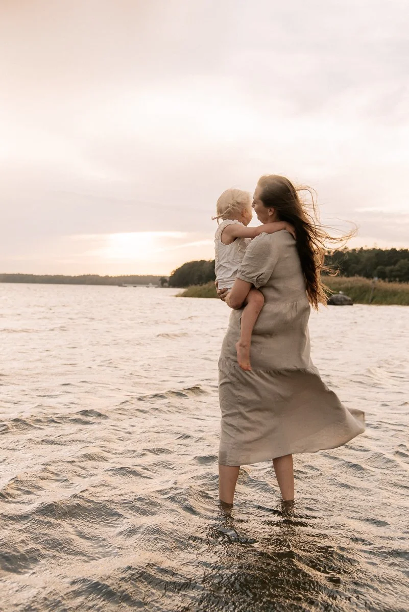 Perhekuvaus Helsinki, äiti kävelee meressä ja kantaa sylissään lasta.
