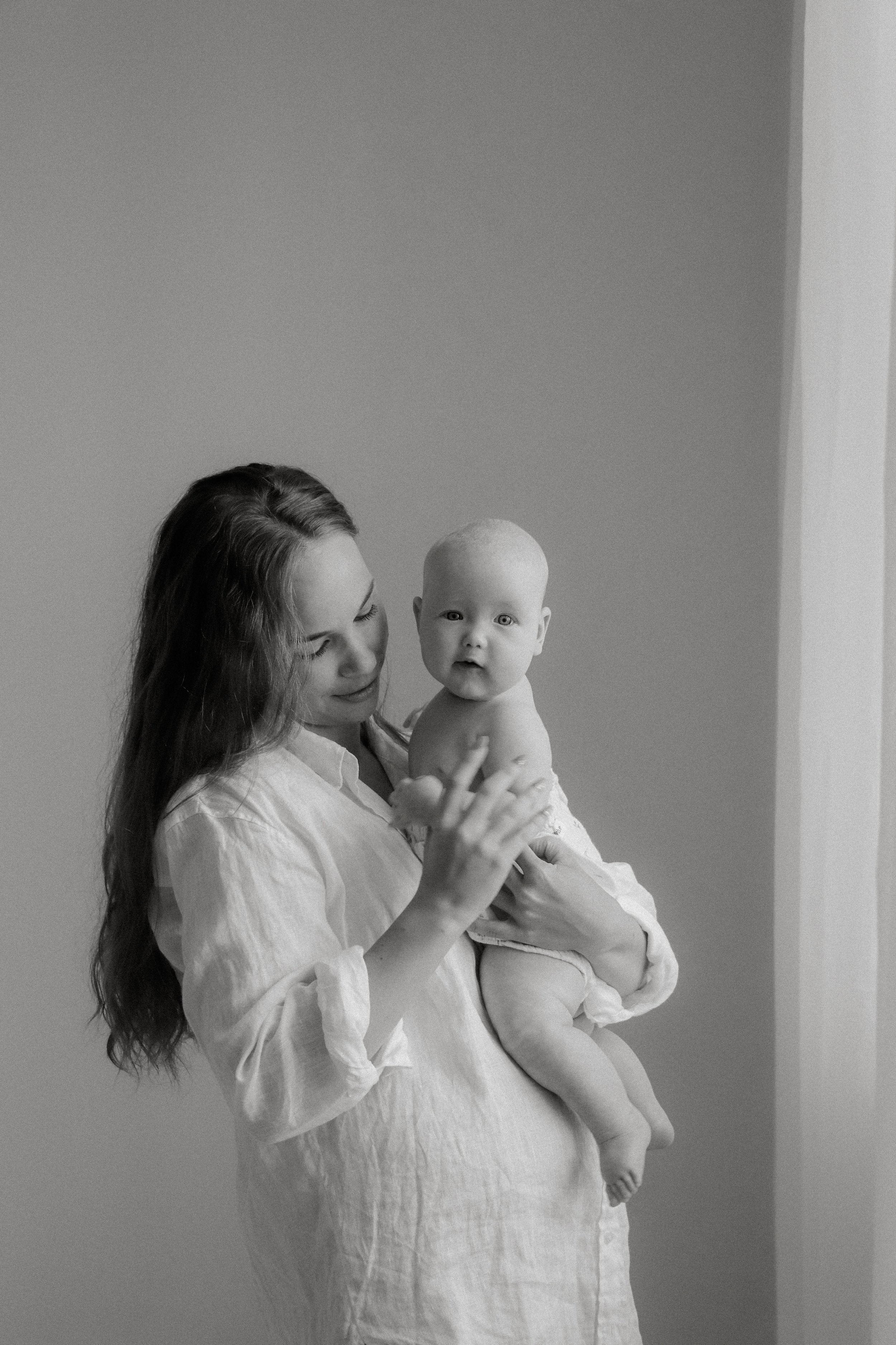 Äiti pitelee lastaan hellästi sylissä. Äiti- ja lapsikuvaus studiolla.