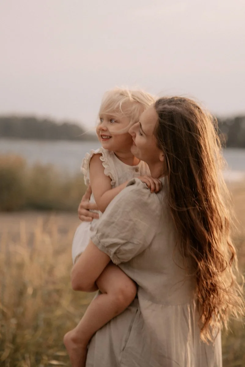 Äiti halaa lastaan tunnelmallisessa perhekuvassa ilta-auringossa.