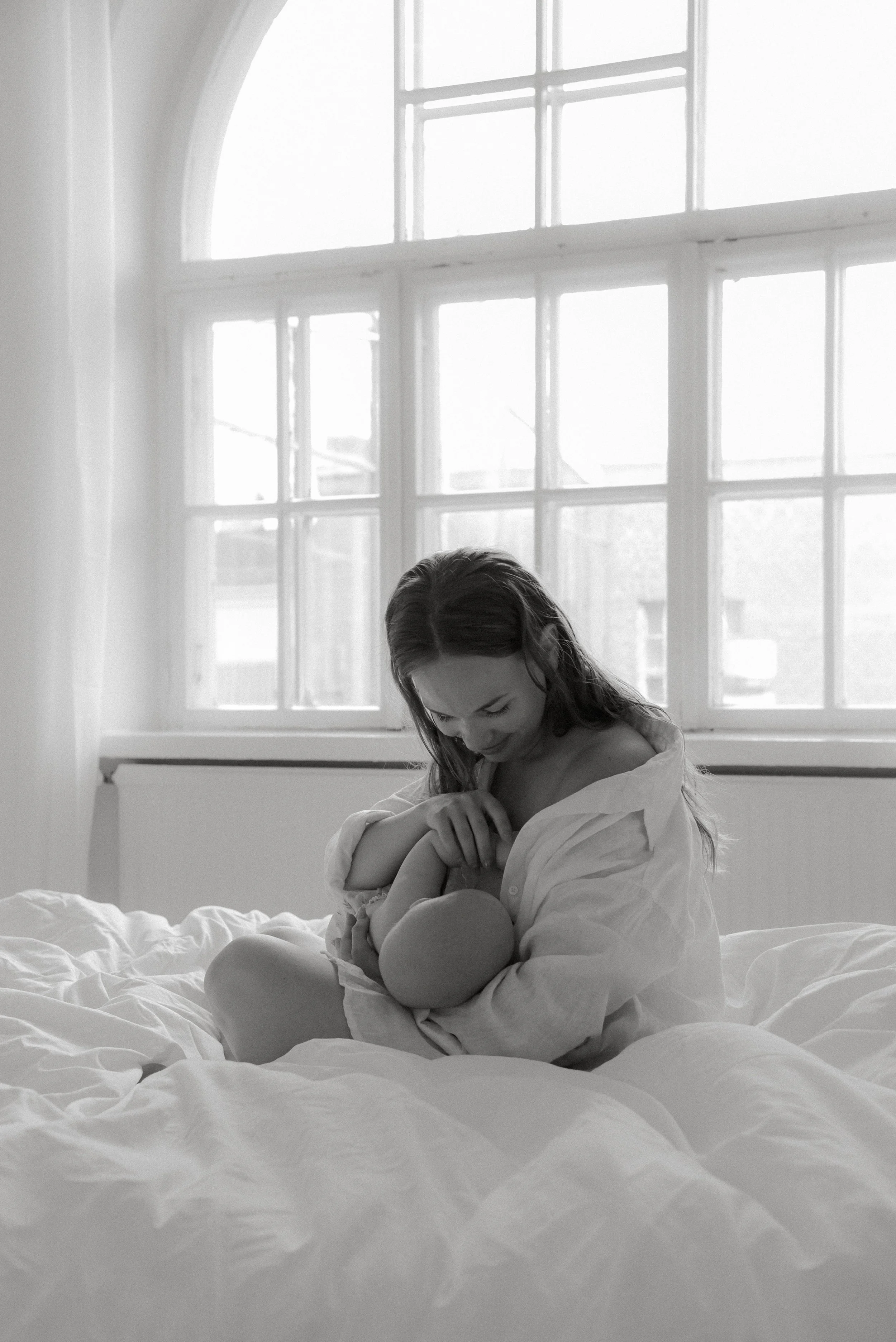 Vauva äidin sylissä Heidi Väisäsen valokuvausstudion sängyssä. Taustalla iso ikkuna, josta tulvii valoa studiolle.