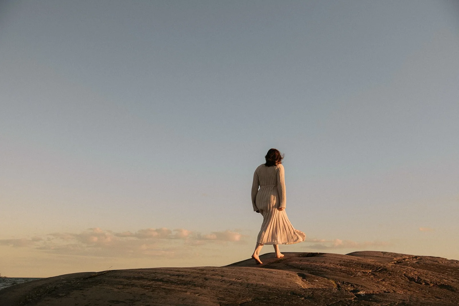 Odottava äiti kävelee ilta-auringossa kalliolla. Odotusajankuvaus Helsinki.