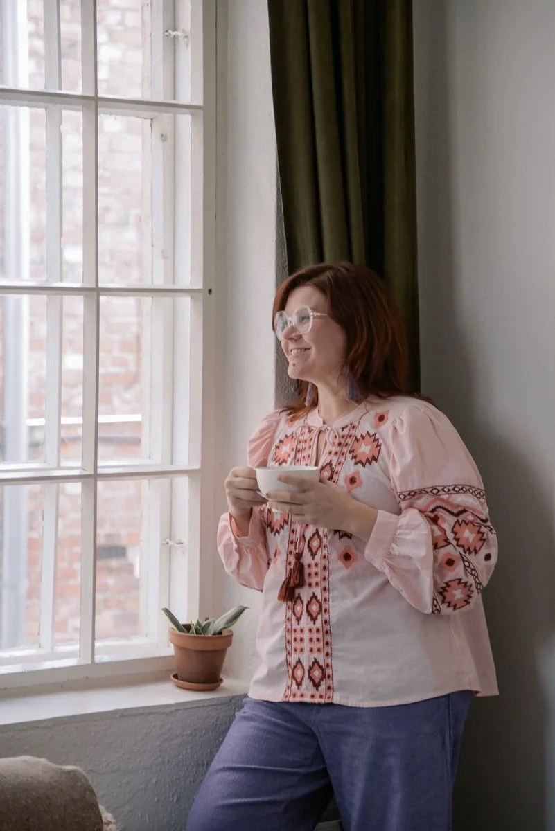 Verhoomo Vanhan Viehätys yrityskuvaus, naisyrittäjä Virve Taljavirta pitelee kädessään teekuppia ja katsoo hymyillen ulos ikkunasta.