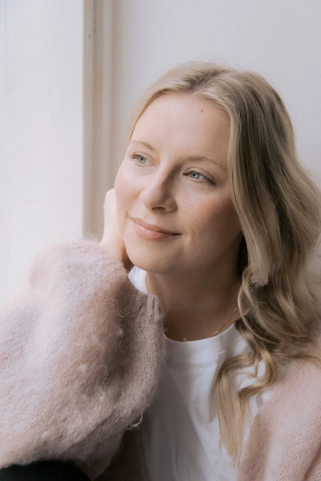 Henkilökuva doula Jutta Alasesta. Naisyrittäjä mietteliäänä ikkunan edessä luonnonvalossa.