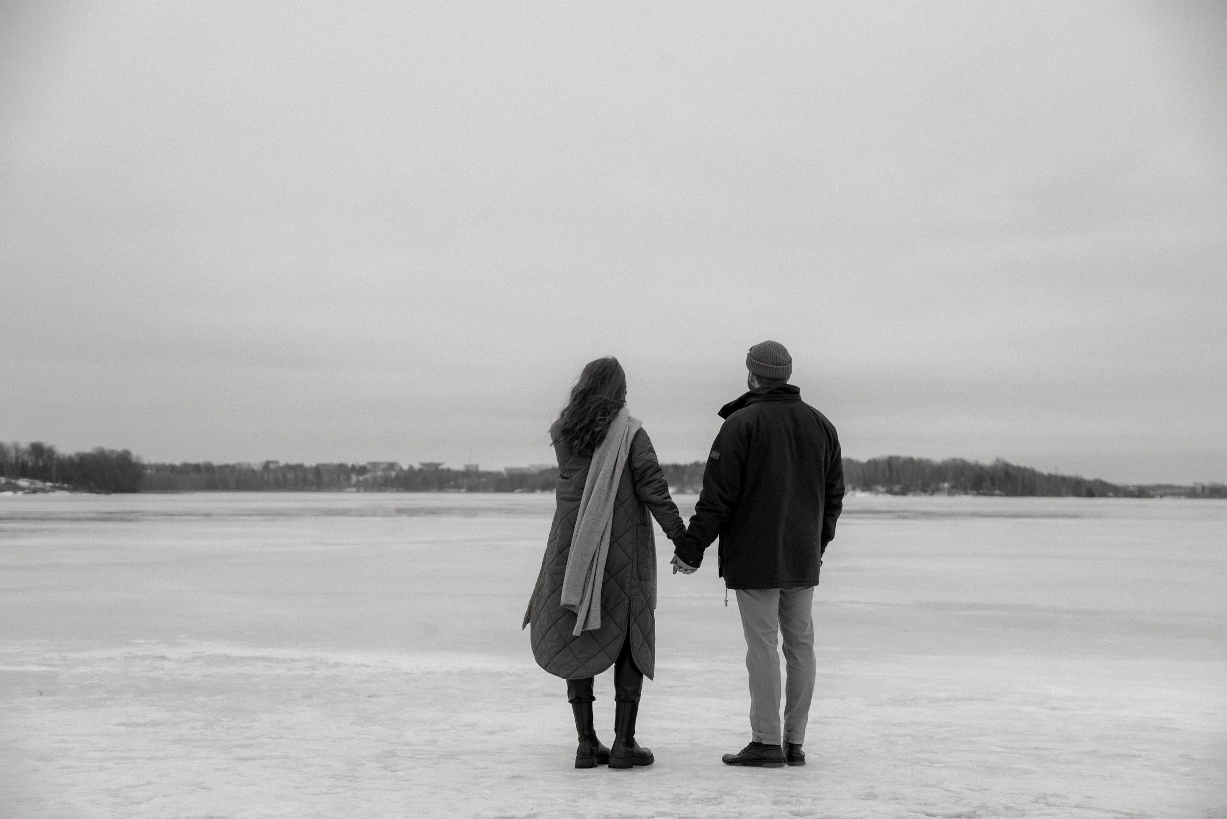 Nainen ja mies käsi kädessä järven jäällä. Pariskuntakuvaus Lauttasaari.