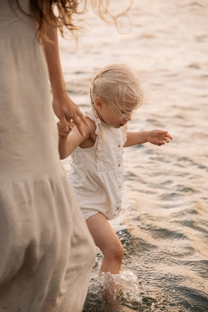 Perhekuvaus meren äärellä, äiti ja pieni lapsi kahlaavat vedessä. Kuvannut valokuvaaja Heidi Väisänen.
