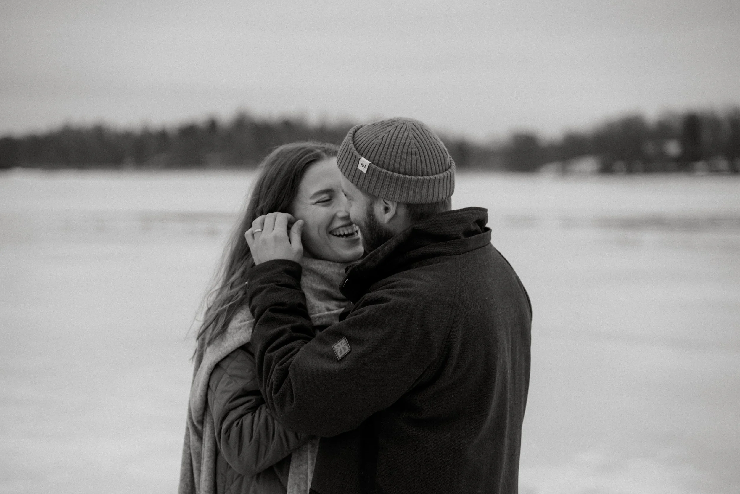 Luonnonvalossa kuvattu mustavalkoinen valokuva, jossa pariskunta katsoo toisiaan ja hymyilee. Pariskuntakuvaus Helsinki.